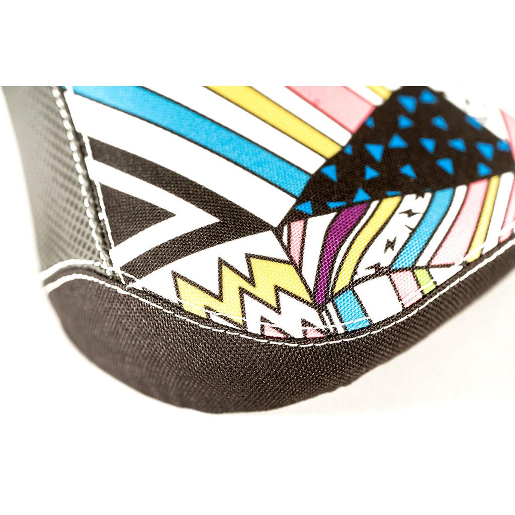 The Colony X Fist Pivotal Seat showcases a vibrant geometric pattern with black, yellow, pink, blue, and white zigzags, triangles, and stripes on extra grippy fabric. White stitching adds style and comfort around the edges of this BMX seat.