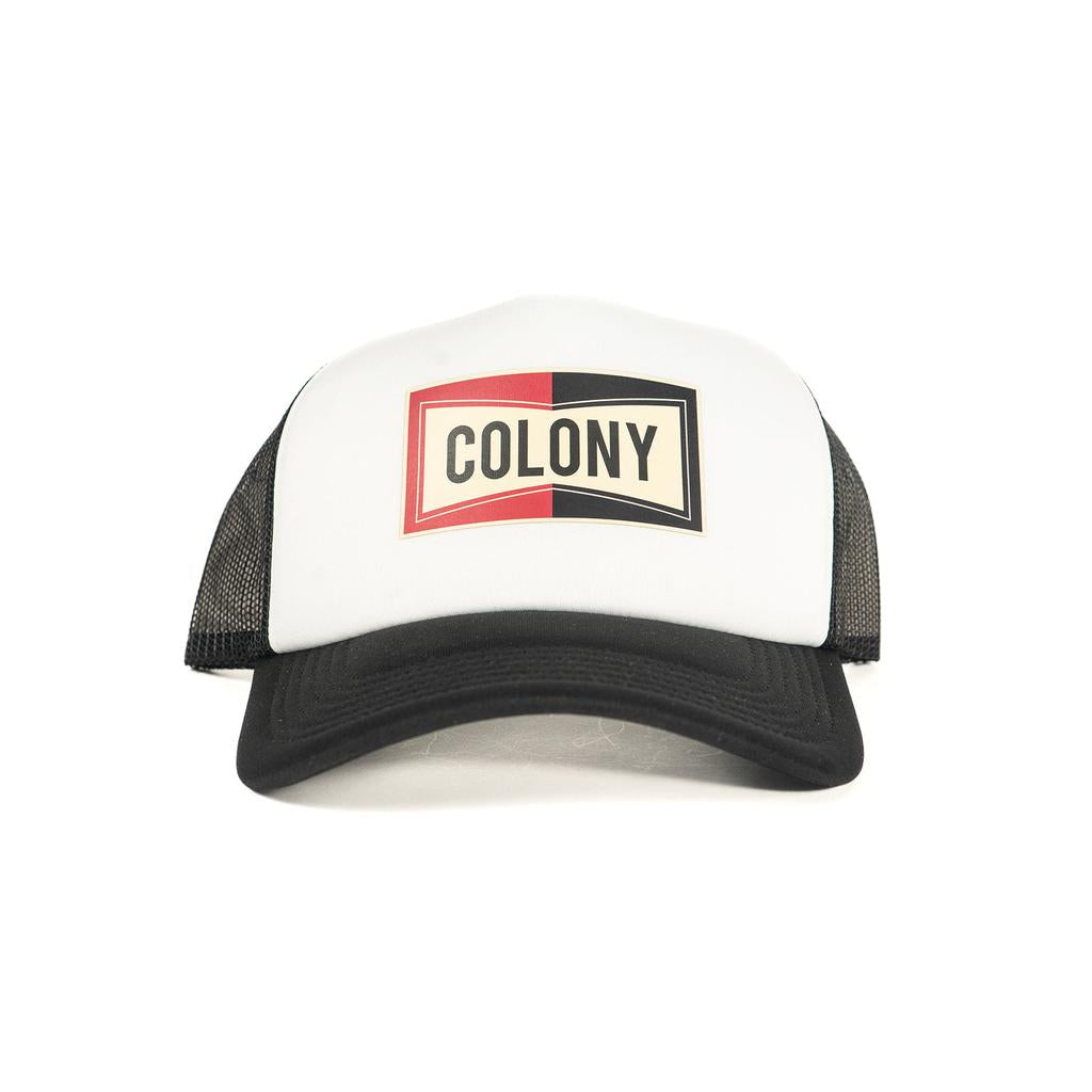 The Colony Champion Trucker Cap is a stylish hat with a bold red and black logo featuring the word "Colony." Made from recycled polyester mesh, this white and black cap combines classic design with modern sustainability.