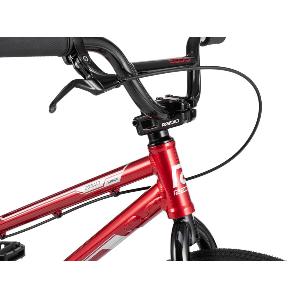 Close-up of a red BMX race bike's front section, highlighting the handlebars, brake cables, and frame markings. The brand "Radio Raceline" and model name "Radio Cobalt Junior Bike" are prominently visible.