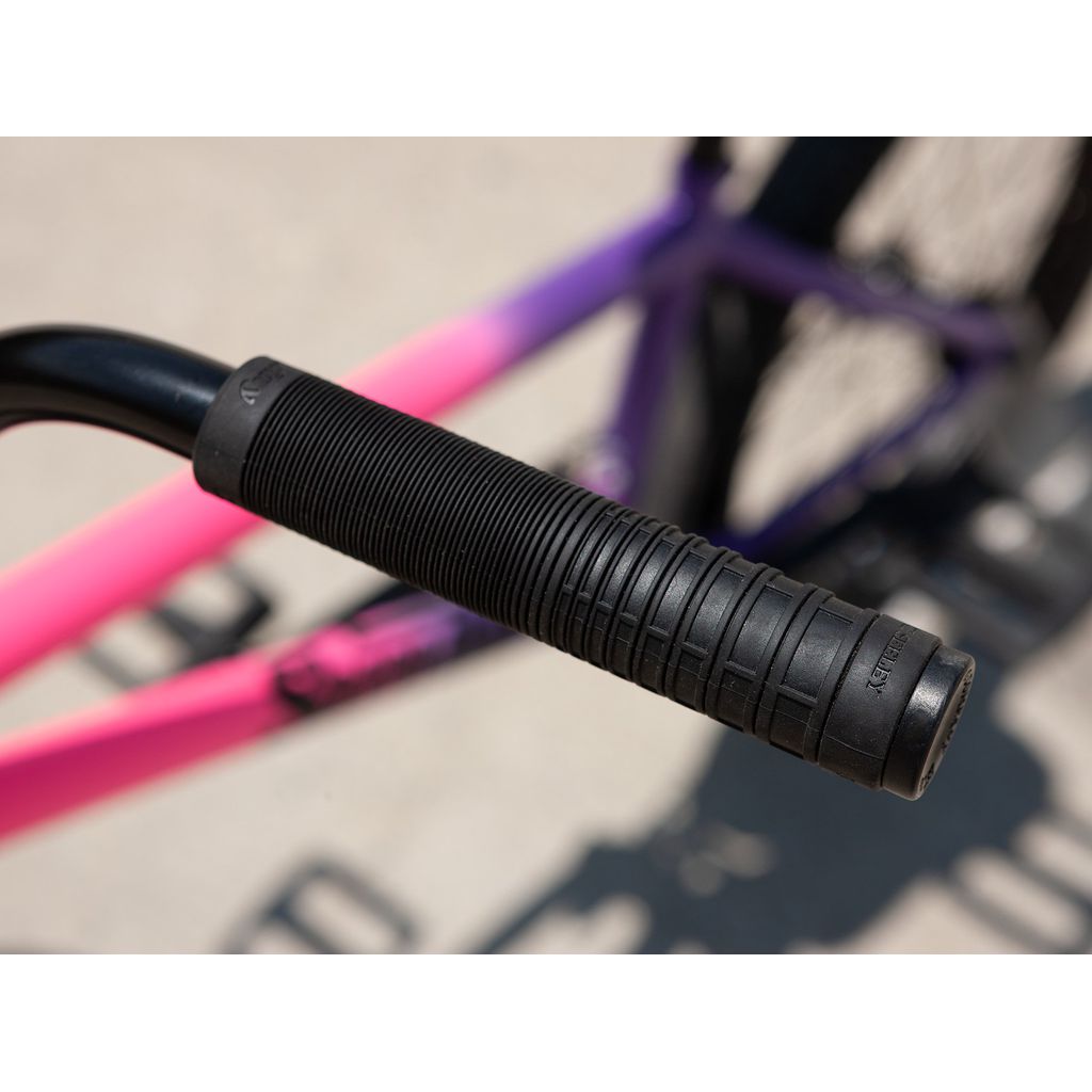 Close-up of the handlebar on the Sunday Street Sweeper 20 Inch Bike with its black rubber grip, highlighting its robust design. The partially visible chromoly frame showcases a pink to purple gradient.