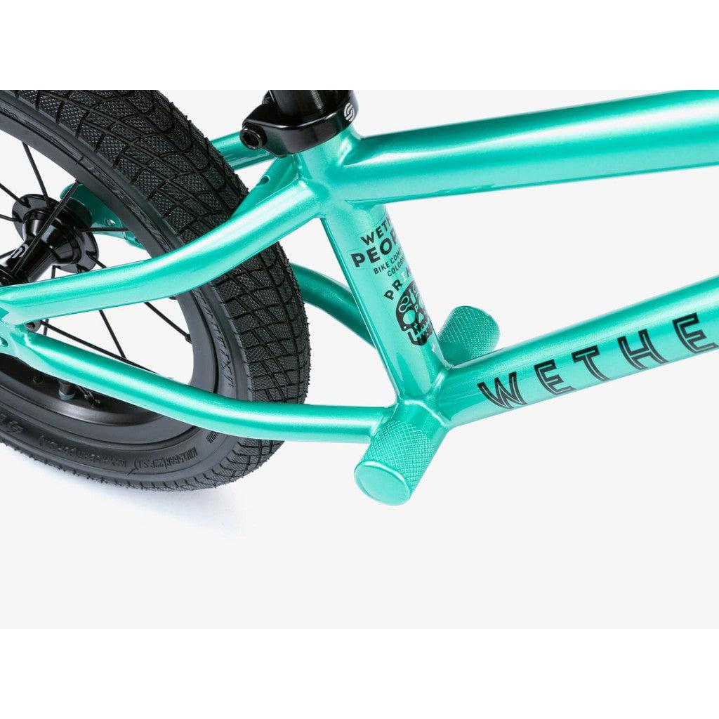 Close-up of a teal Wethepeople Prime Balance BMX Bike frame with branding, emphasizing its textured pegs and black tires. This model exemplifies high performance and style in perfect harmony.