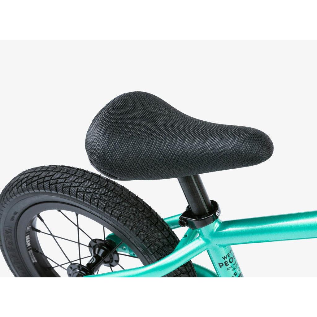 Close-up of a black bicycle seat and rear wheel on a teal Wethepeople Prime Balance BMX Bike, featuring textured tire and visible spokes that highlight its craftsmanship.