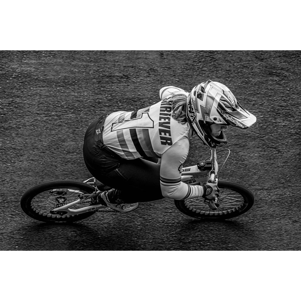 A cyclist in full gear, including a helmet and jersey with "FOREVER" on the back, rides a BMX bike on a paved surface at the 2024 National BMX Championships. The image is part of the LUXBMX Race Photo Package and is in black and white, capturing the intensity of the race.