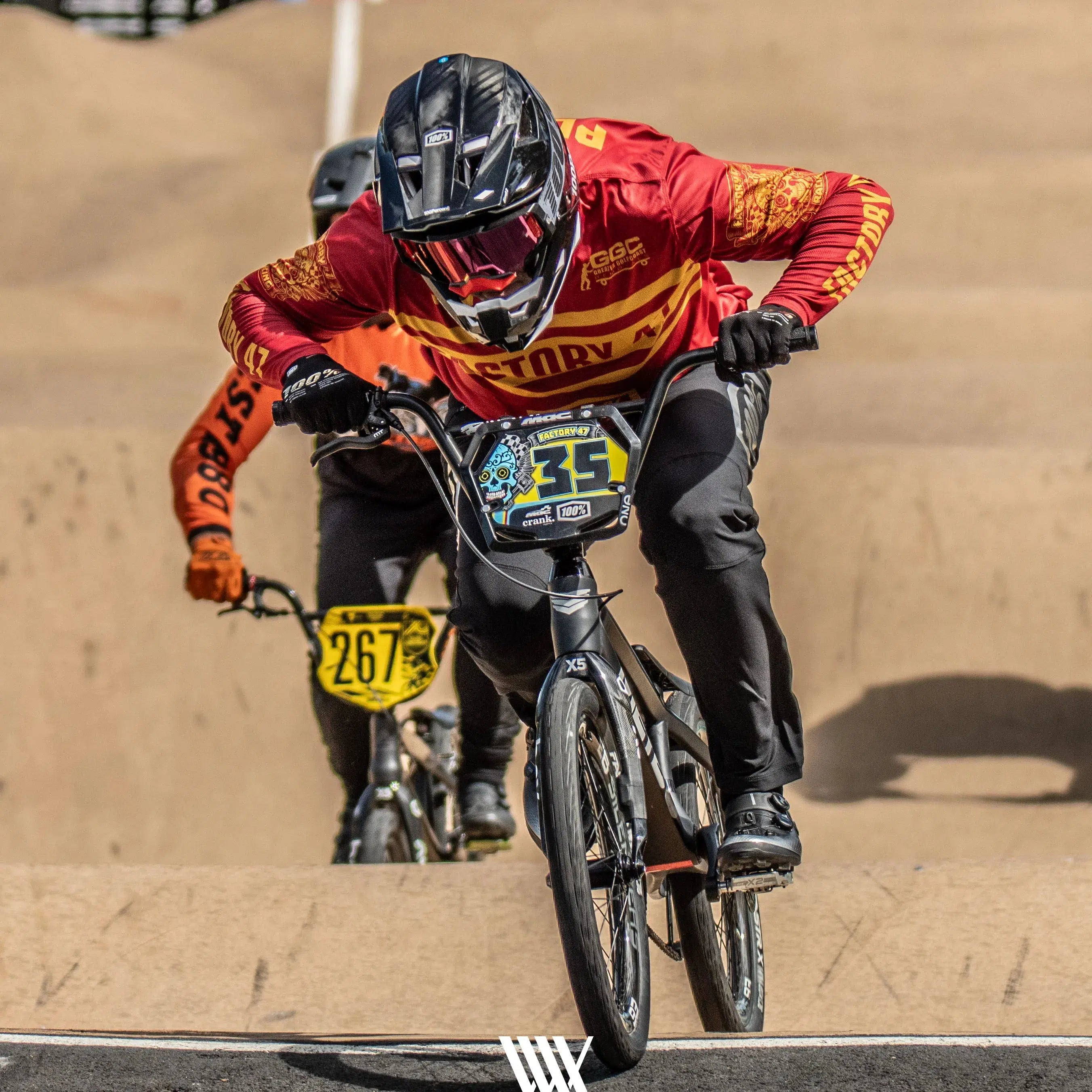 Two cyclists race on a BMX track at the 2024 Perth Championships. The cyclist in front, wearing a red and orange jersey with the number 357, leads while the cyclist behind, in a yellow jersey with the number 267, strives to catch up. Captured by LUXBMX's team as part of their Race Photo Package: 2024 National BMX Championships, these BMX race photos are electrifying.