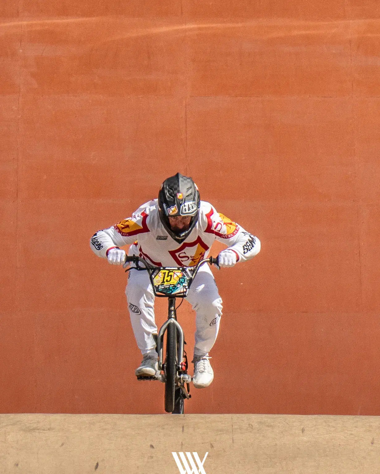 In an electrifying scene echoing the thrill of the 2024 National BMX Championships, a cyclist in a white and red outfit and helmet launches off a ramp on their BMX bike. The action is captured vividly against an orange backdrop, reminiscent of iconic race photos from the LUXBMX Race Photo Package.