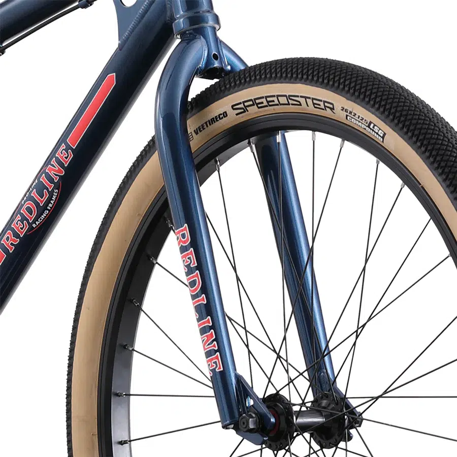 Close-up of a blue 26-inch front wheel from the Redline SQB bike, highlighting a beige tire with "SPEEDSTER" on the sidewall and the "REDLINE SQB" brand name displayed on the fork.