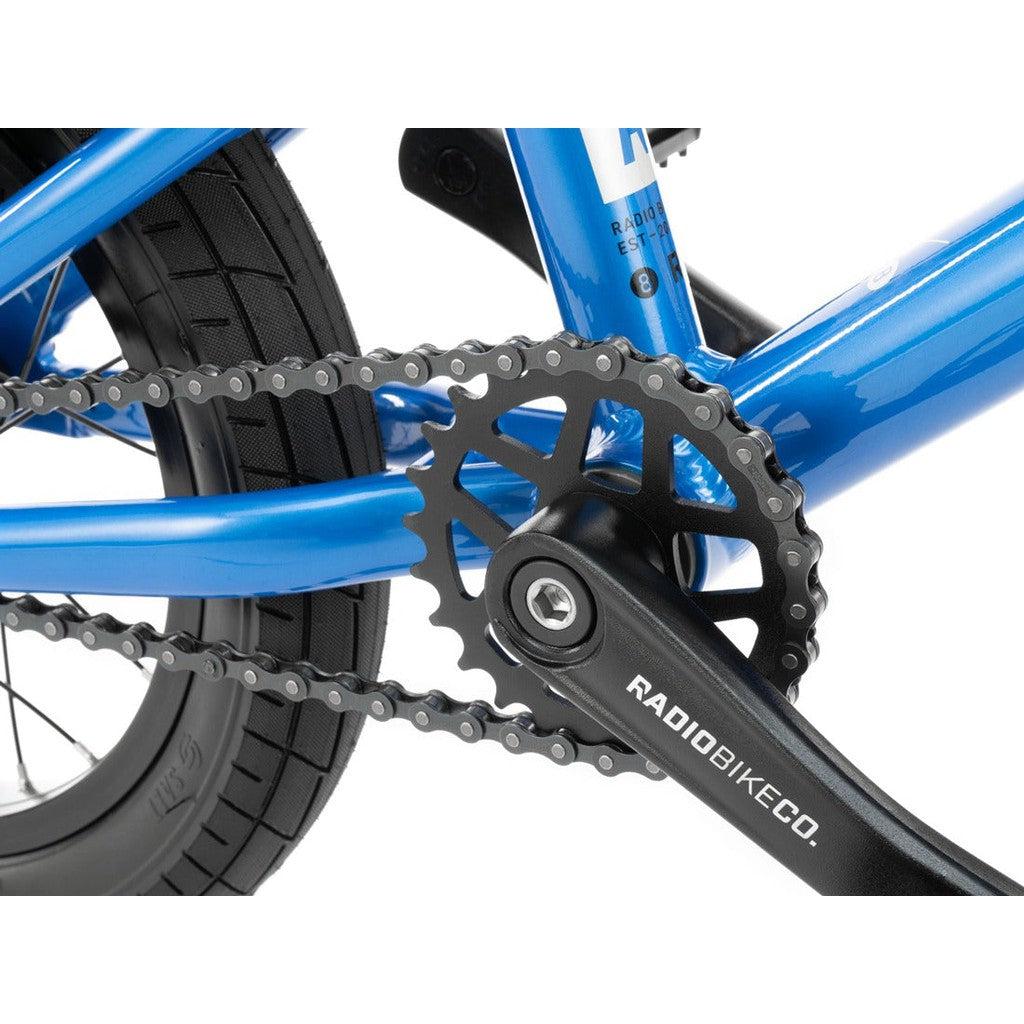 Close-up of the crankset, chain, and rear wheel of a blue Radio Dice 14 Inch Bike, showing the pedal arm labeled "RADIOBIKECO," crafted from lightweight 6061-T6 alloy. Perfect for a kids bike!