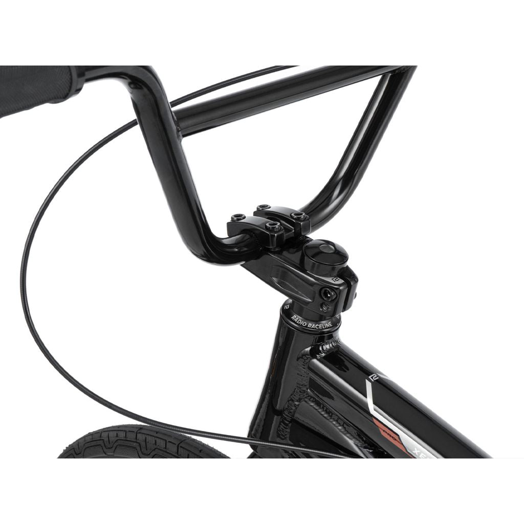 Close-up of a black Radio Xenon Pro Bike handlebar and stem, showing the front brake cable and part of the front wheel on this sleek race bike.