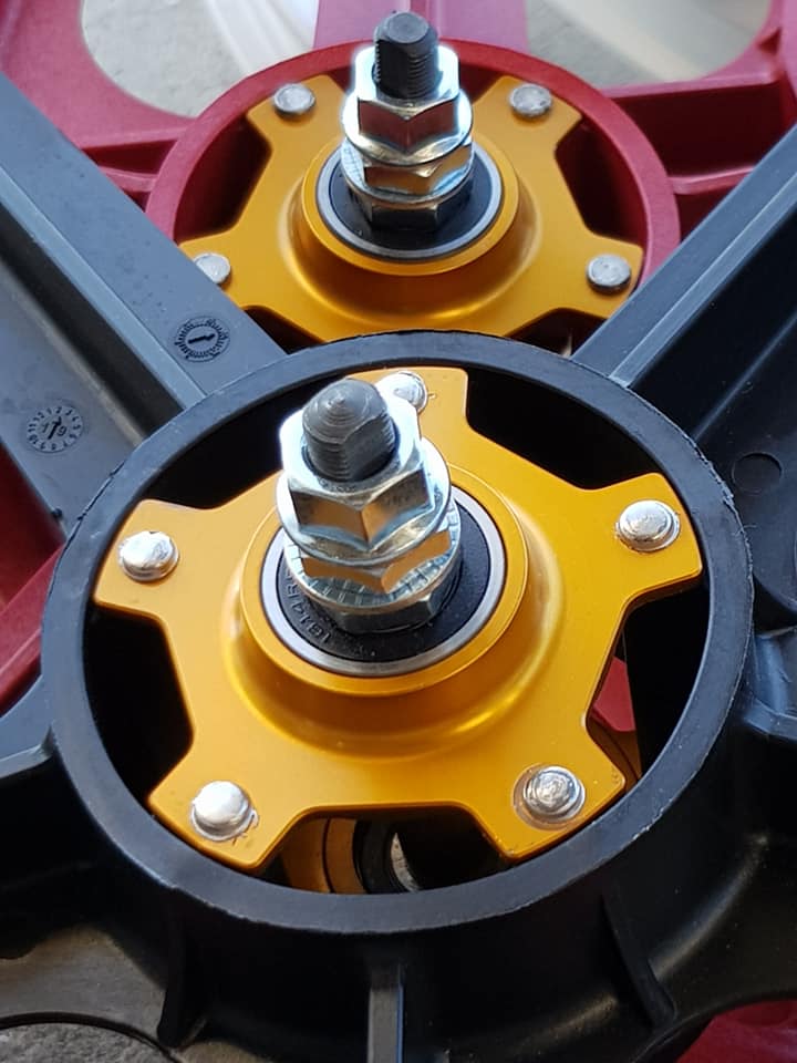 A close-up of two metallic mechanical components features yellow and red accents, ideal for retro rebuilds. Bolts and washers are visible on each piece, echoing the look of Skyway Tuff II Rivet 20 Collectors Edition Wheelset for a classic BMX bike appearance.