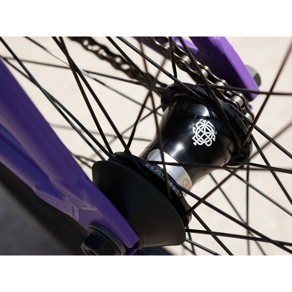 Close-up of a Sunday Street Sweeper 20 Inch Bike wheel showcasing a black hub and purple chromoly frame, featuring intricately intertwined metal spokes.