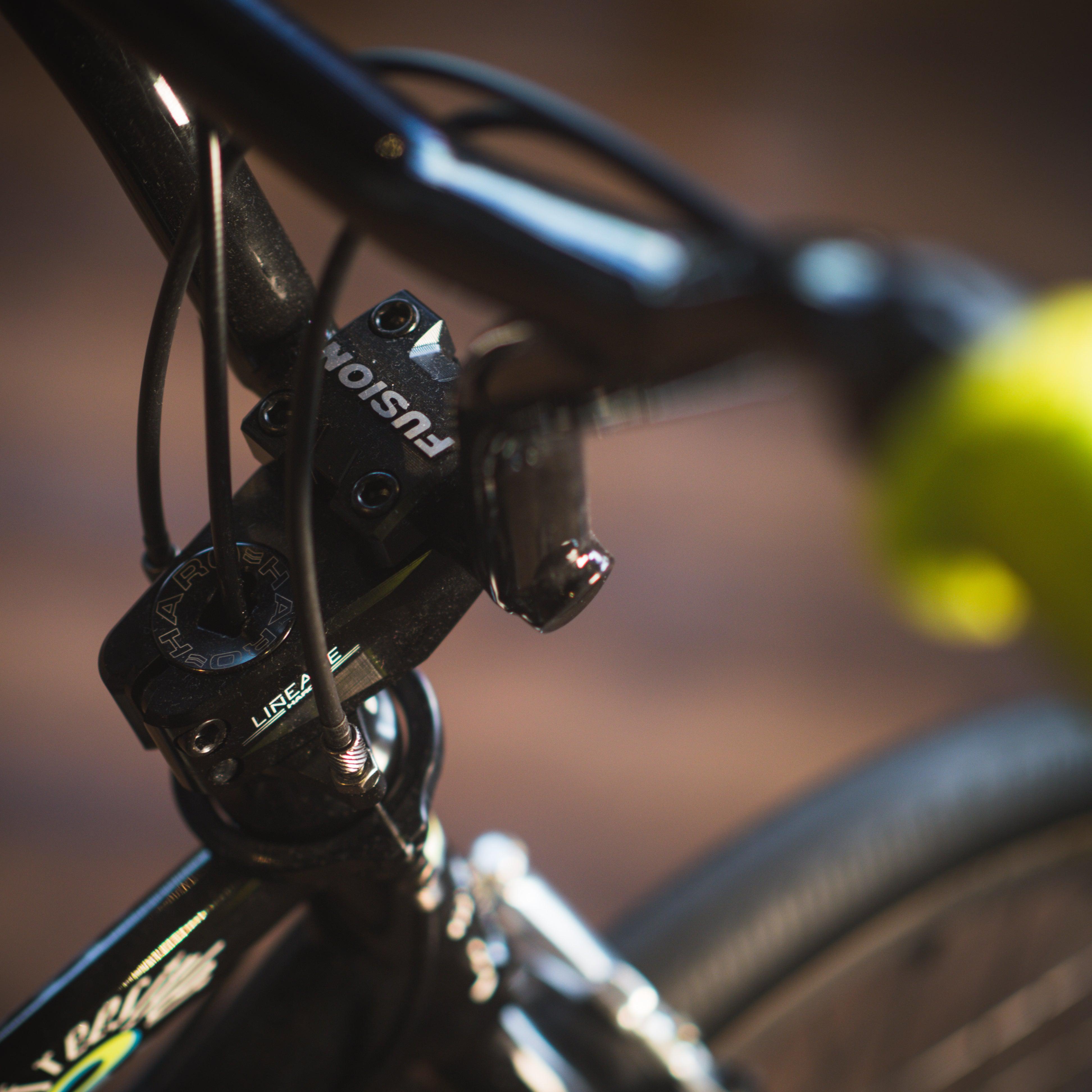 Close-up of the Haro Lineage Sport Freestyler Bashguard 26 Inch Bike handlebar with "FUSION" visible on the stem under natural light. The black handlebar and stem are connected to the chromoly frame, with a part of the front wheel in view.