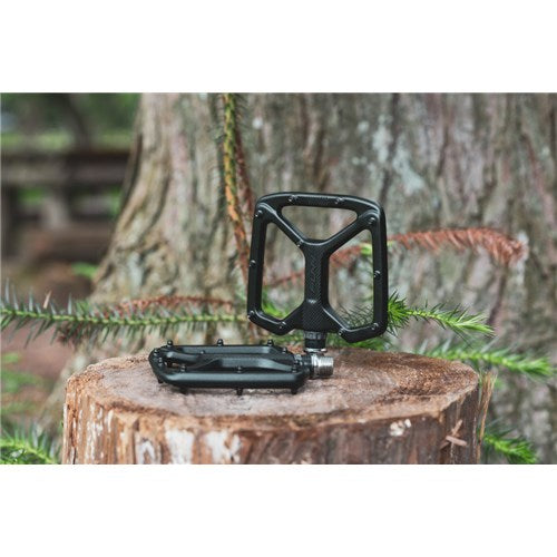 Funn Python V2 Alloy Pedals, crafted from durable AL6061 alloy, rest on a tree stump outdoors with blurred trees in the background.