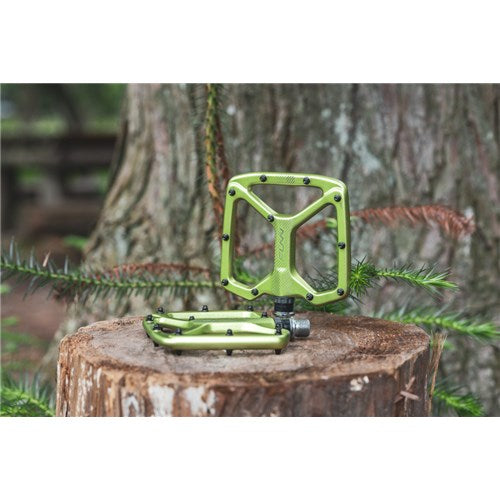 Funn Python V2 Alloy Pedals in vibrant green with grip pins rest on a tree stump, showcasing unmatched stability and performance against the backdrop of tree branches.