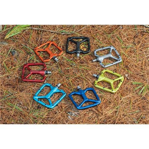 Six vibrant Funn Python V2 Alloy Pedals form a circle on brown pine needles, boosting performance and stability for an exceptional ride.