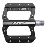 The HT AE12 Pedals are black with silver accents, featuring the "HT" logo and "AE12 L" markings. Made with a CNC aluminium body and EVO+ system, they include multiple screws for better traction.