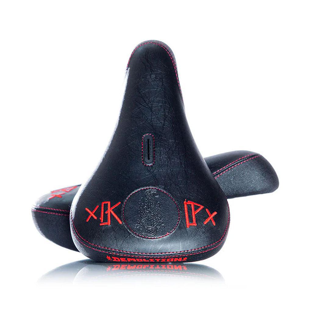 The Demolition Kevin Peraza Seat is a black Pivotal bicycle seat featuring red stitching and unique Demolition logos, inspired by Kevin Peraza's signature style.