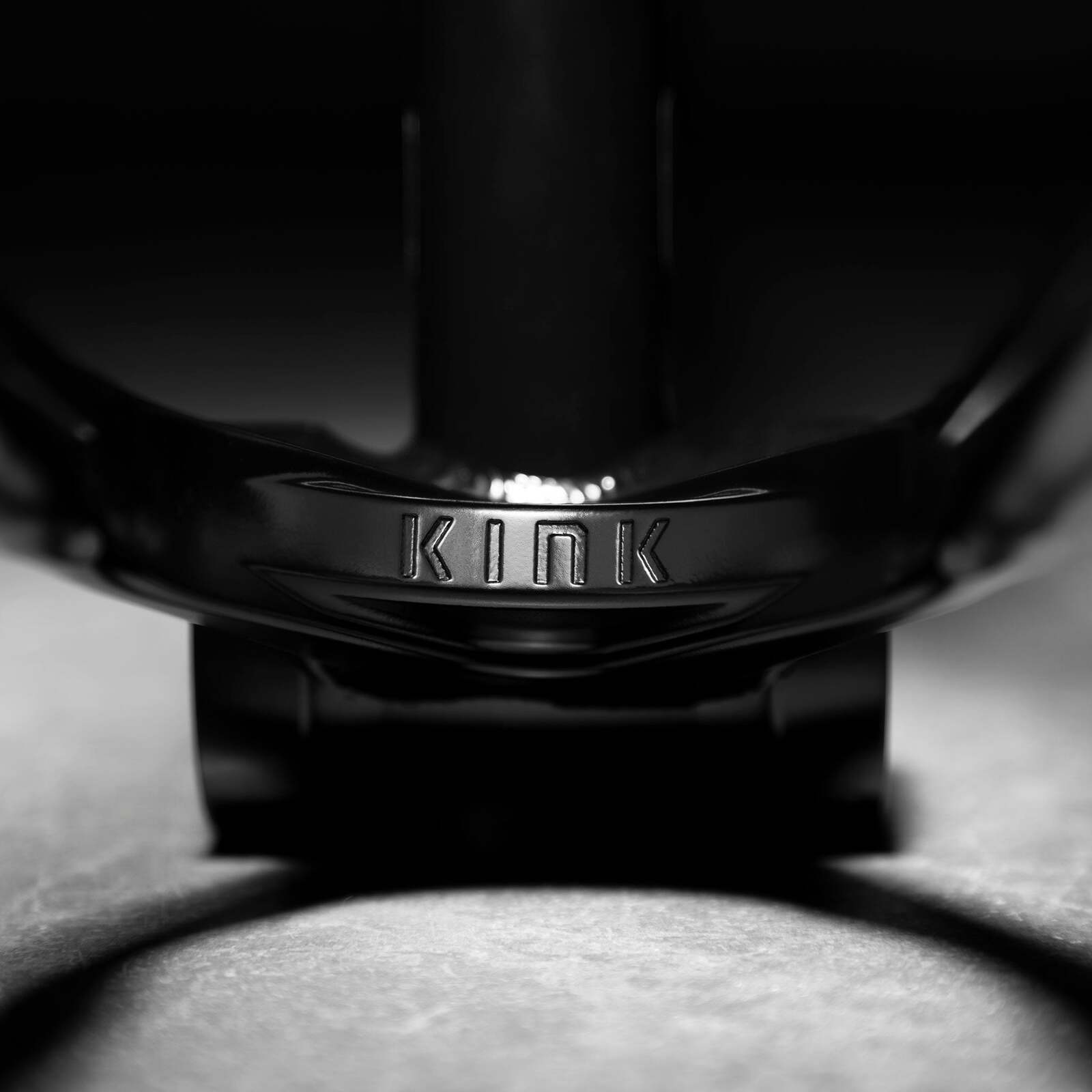 A close-up of a black BMX bike component, engraved with "KINK," casts dynamic shadows. Its street geometry showcases the sturdy Kink Roll Up Frame, a favorite among riders like Hobie Doan.