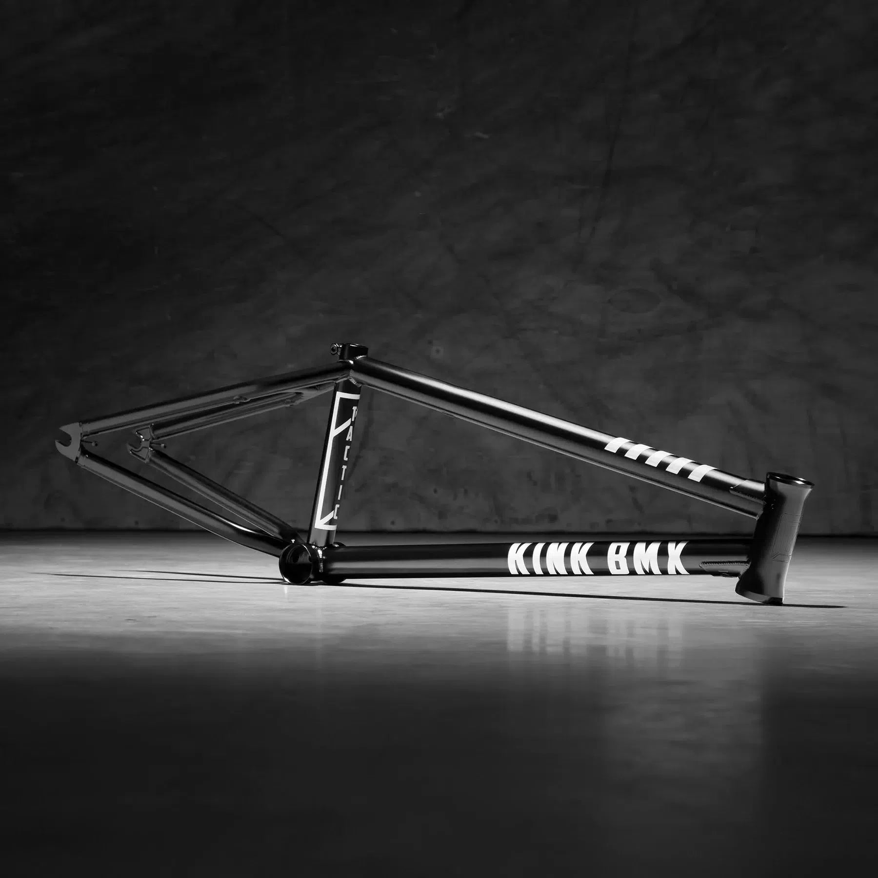 A black BMX street frame called "Kink Tactic Frame" features chromoly tubing and sits on a concrete surface with a textured gray backdrop.