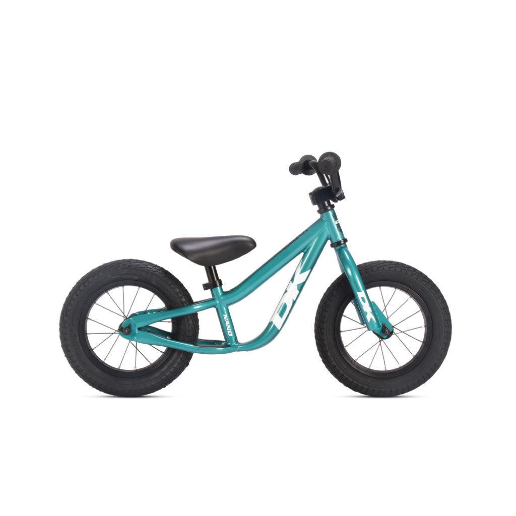 The DK Nano Balance Bike is a small, teal beginner's BMX bike with black handlebars, seat, and tires. The frame features "DK" written in white, making it perfect for young children starting to learn balance and coordination.