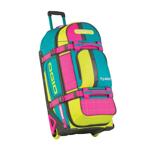 The Ogio Gear Bag / Miami Vice is a vibrant rolling duffel featuring green, pink, and blue sections with straps, wheels, and "Ogio" branding. It includes the SLED System for ultimate gear protection during travel.