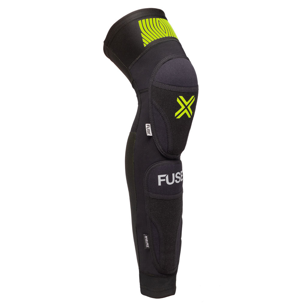 A black and grey Fuse Omega 100 Knee Shin Ankle Combo Pads with green accents, featuring the brand name "FUSE" and a yellow "X" symbol, also includes durable Kevlar sections for added protection.