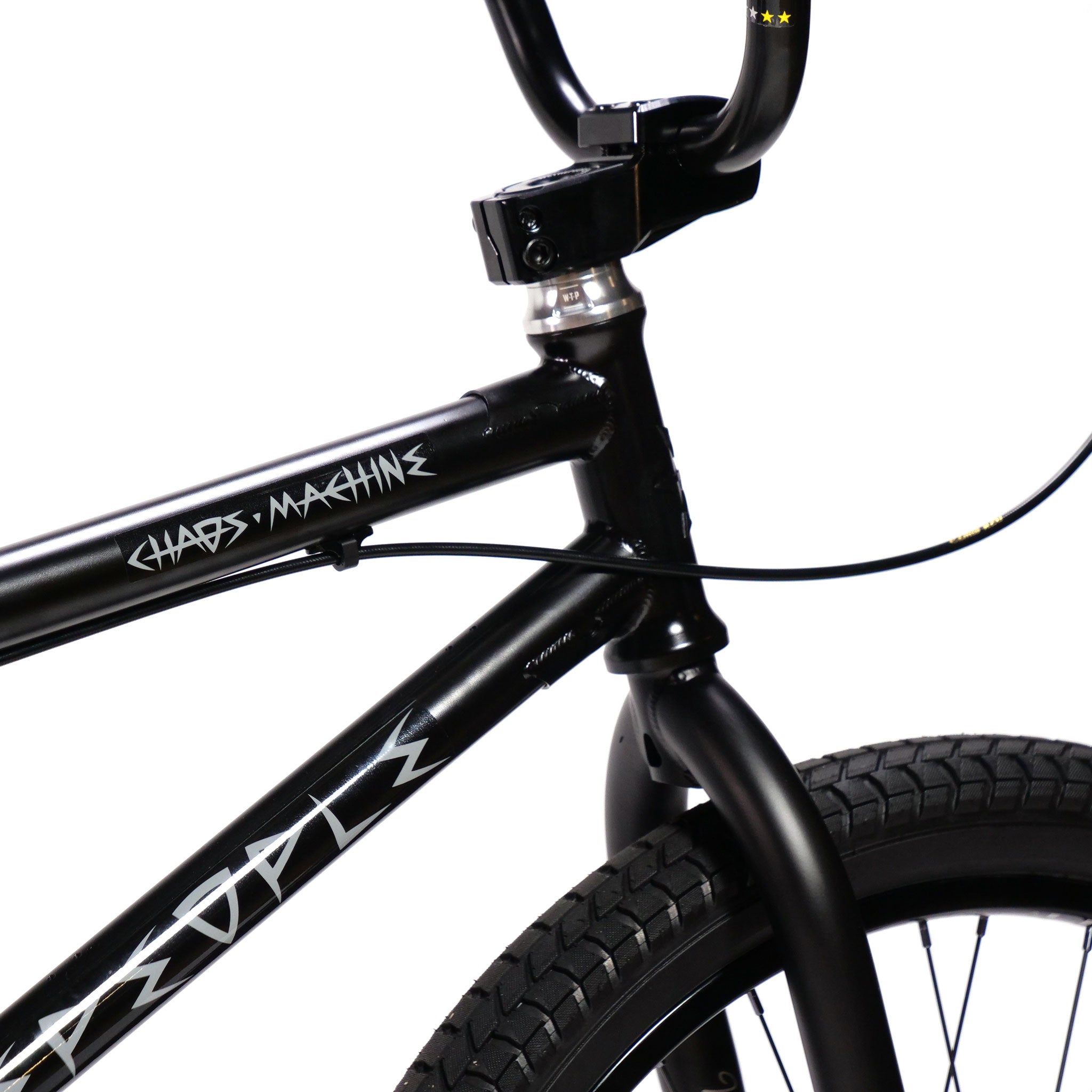 Close-up of the front part of a black Wethepeople Chaos Machine 22 Inch Custom Bike with a "Chaos Machine" label on the 22 Inch Tyson Jones-Peni Frame and handlebars featuring a small gear detail.