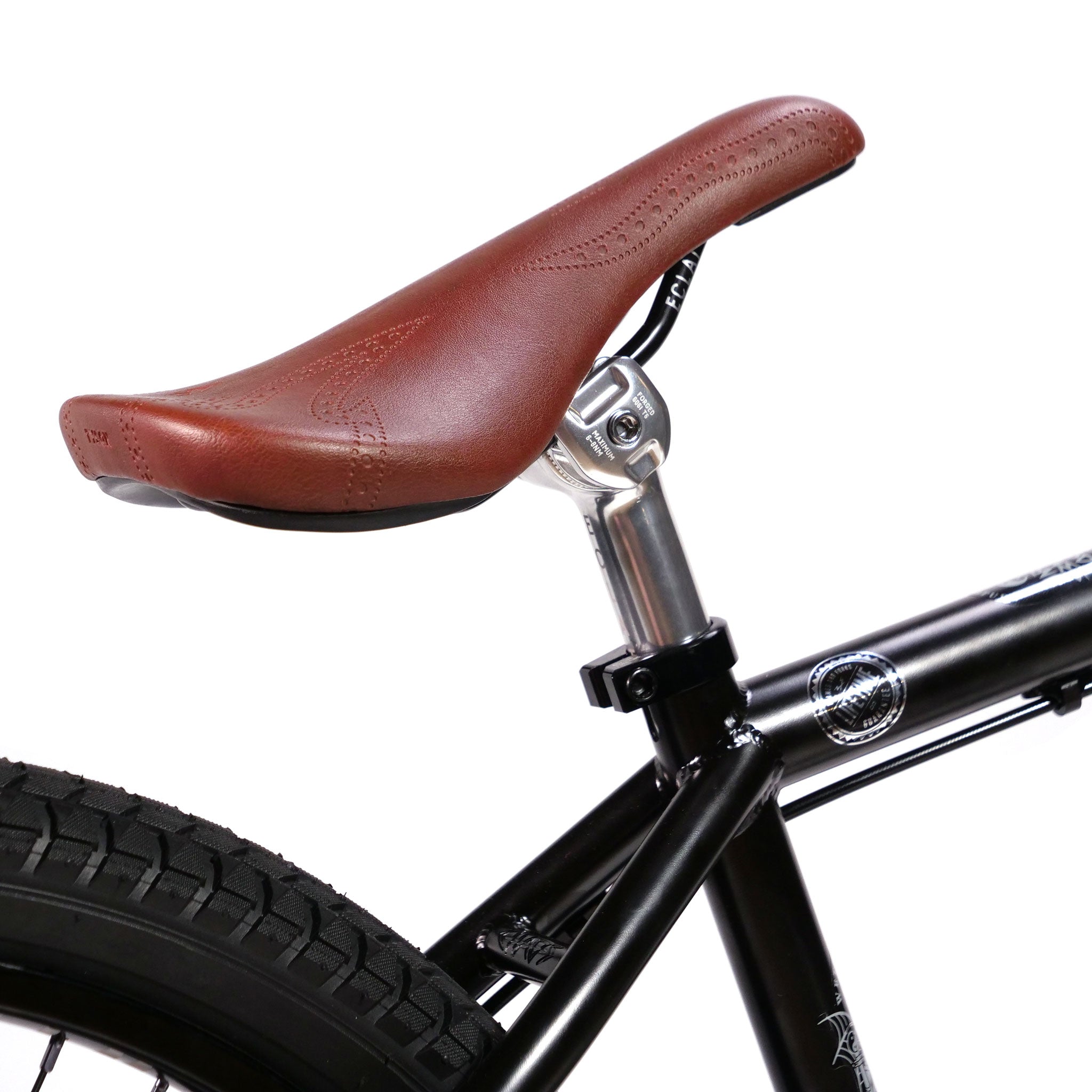 Close-up of a brown bicycle seat attached to a black Wethepeople Chaos Machine 22 Inch Custom Bike. The tire and part of the bicycle's frame are visible.