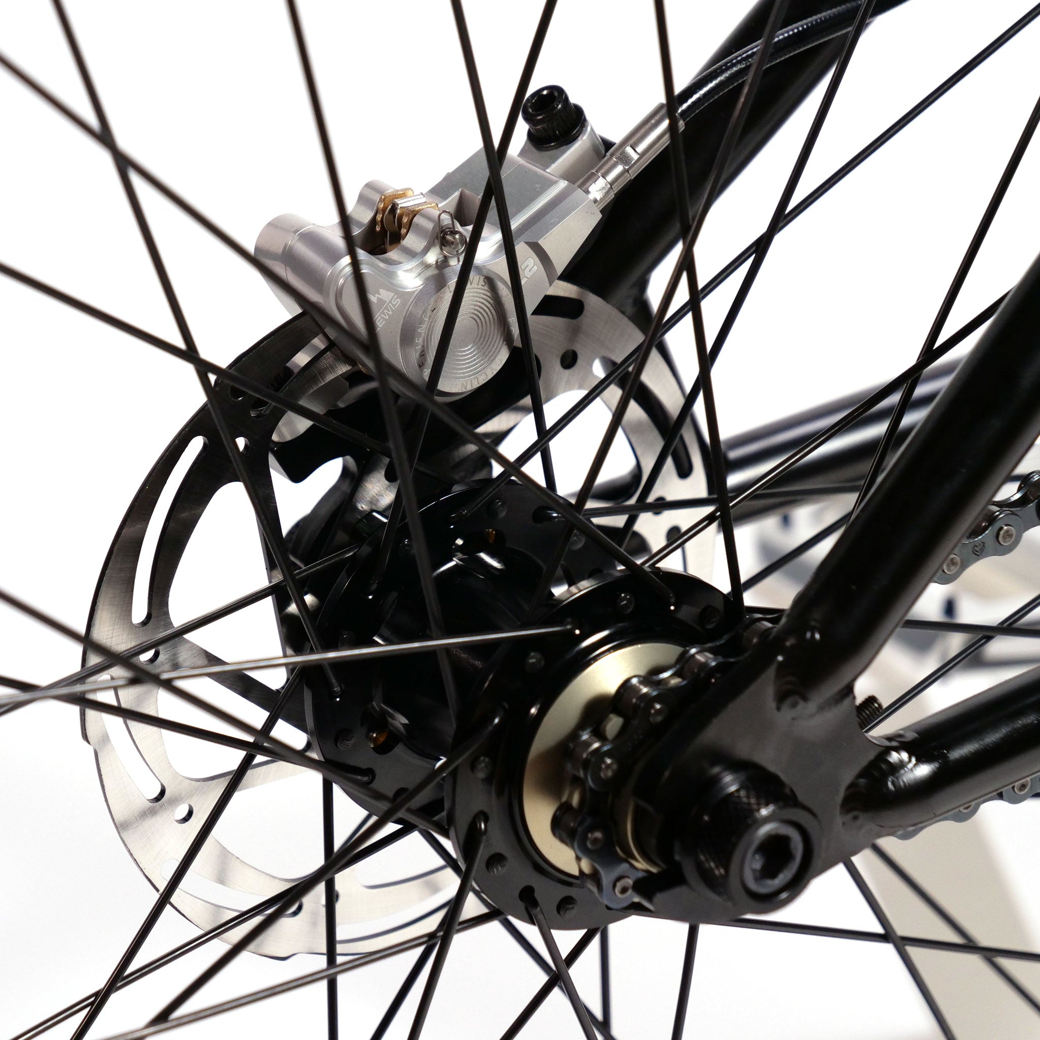 Close-up of a bicycle's disc brake system on a Wethepeople Chaos Machine 22 Inch Custom Bike, showing the brake rotor, caliper, and spokes. The components are attached to the black rear wheel hub.