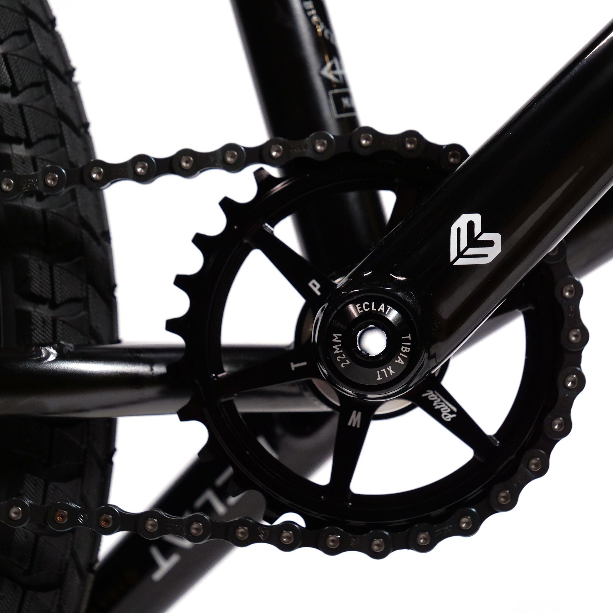 Close-up of a black Wethepeople Chaos Machine 22 Inch Custom Bike's pedal, chainring, and part of the rear tire. The chainring has branding and text visible, including "Éclat Exile" and "M24".