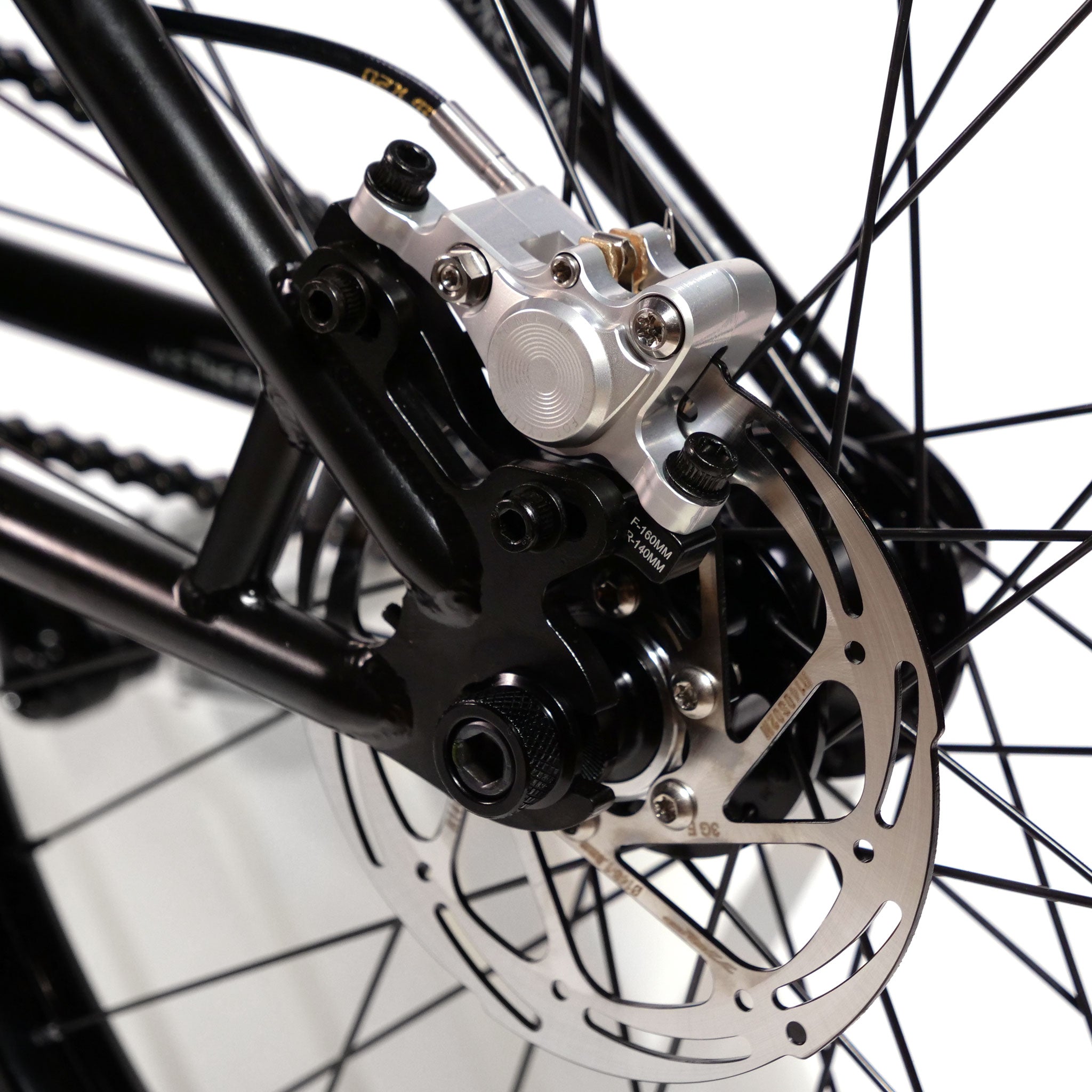 Close-up view of a bicycle's disc brake system, showcasing the caliper, rotor, and spokes in detail. The setup is reminiscent of high-quality models like the Eclat Exile or components found on a Wethepeople Chaos Machine 22 Inch Custom Bike.