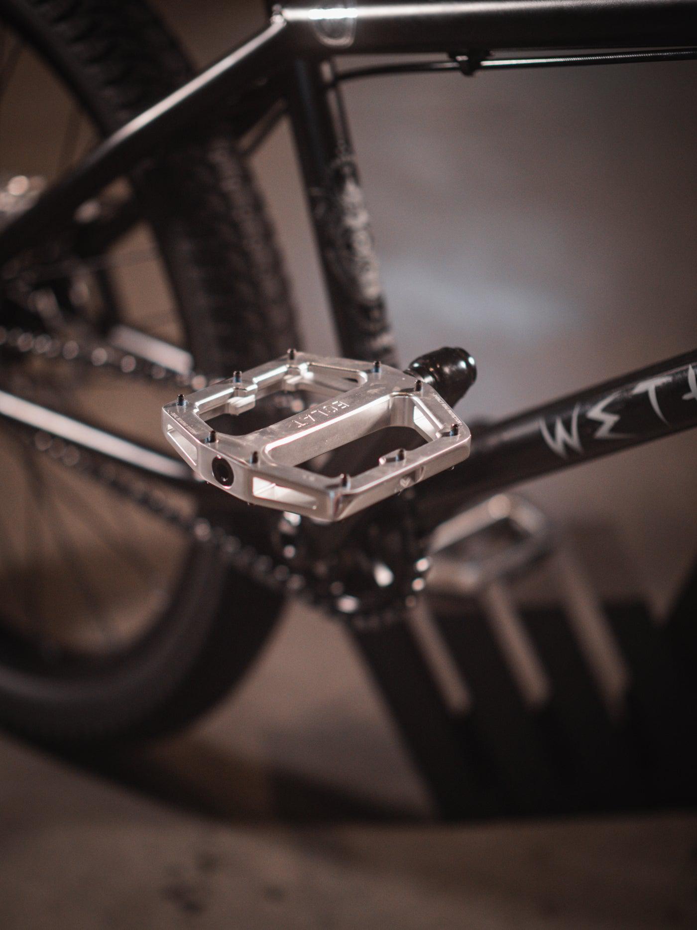 Close-up of a bike pedal attached to a sleek black Wethepeople Chaos Machine 22 Inch Custom Bike frame.