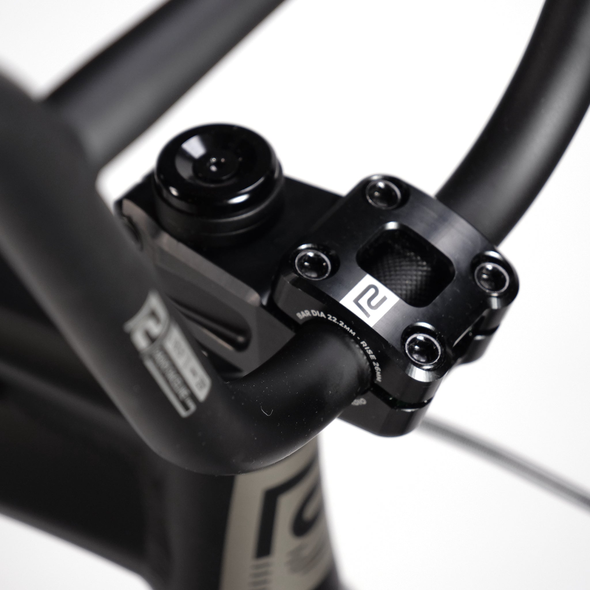 Close-up of a black bicycle handlebar stem assembly with several bolts and branding logos visible, attached to the Radio Quartz Pro XL Bike 2025's lightweight hydro-formed frame.