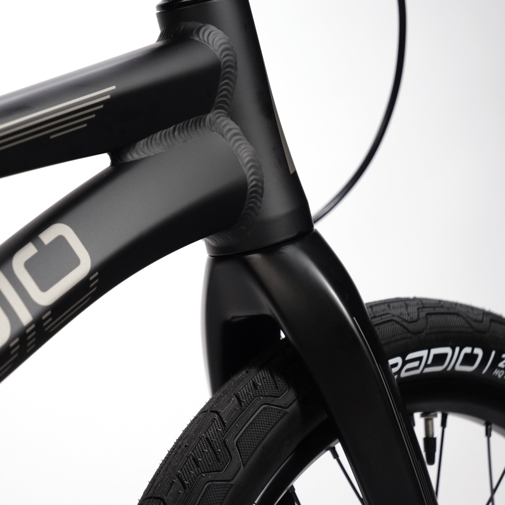 Close-up of the front section of a black Radio Quartz Pro XL Bike 2025, showcasing its handlebars, lightweight hydro-formed frame, and front tire marked with the brand name "RADIO." The bike is equipped with hydraulic disc brakes for superior stopping power.