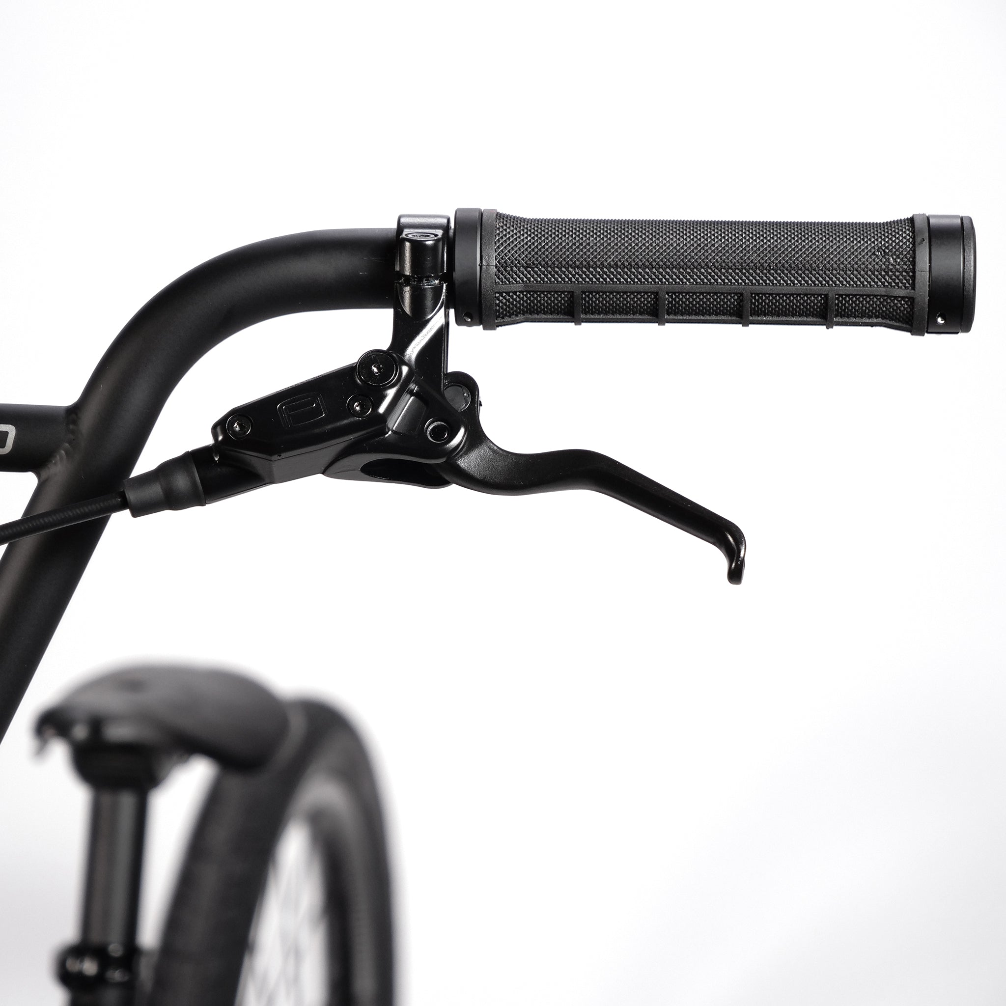 Close-up of the handlebar and brake lever of the Radio Quartz Pro XL Bike 2025, featuring a textured grip, set against a plain white background. The partially visible front tire and fender suggest the sleek design of its lightweight hydro-formed frame.