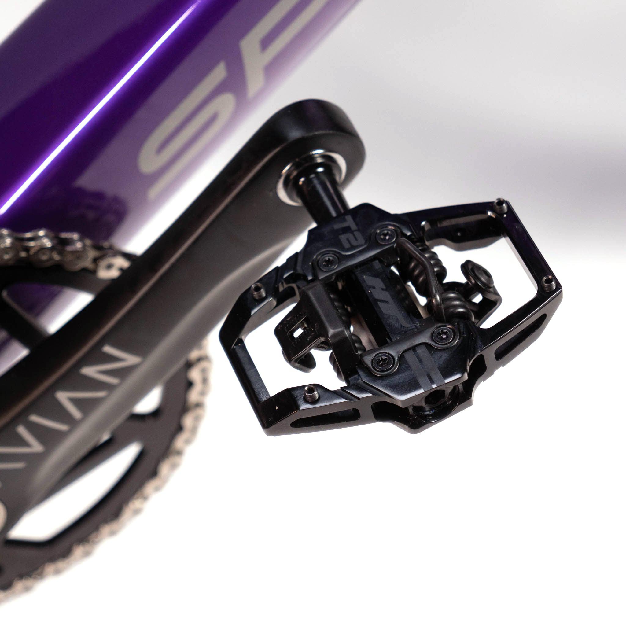 Close-up of a black bicycle pedal attached to a Speedco Velox Evo Pro XXXL Custom Bike purple frame, with a visible part of the chainring.