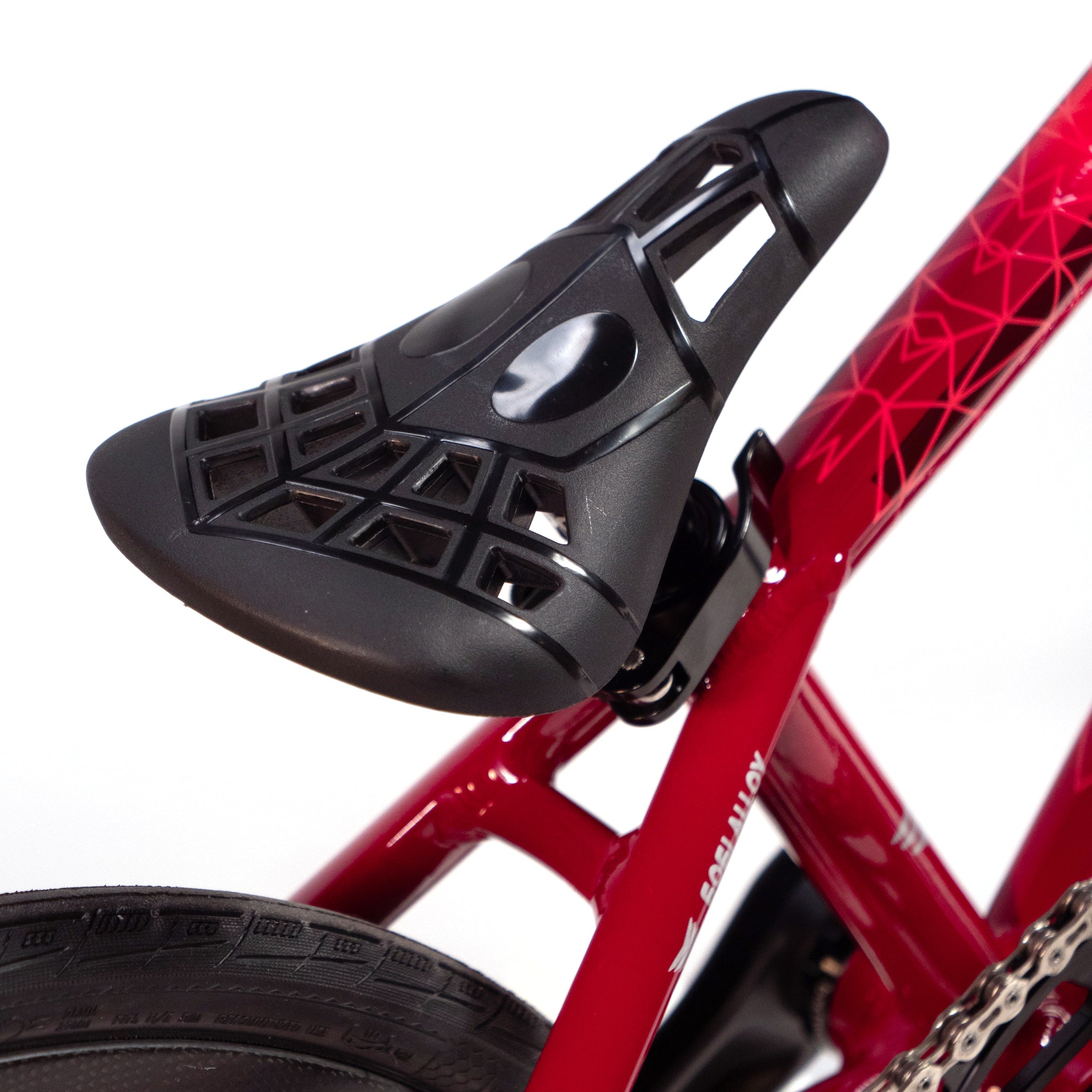 Close-up image of a black bicycle saddle attached to a red frame. The saddle features a geometric cutout design. A portion of the rear tire and part of the bike's chain can be seen, highlighting the precision engineering found in custom race bikes like the Meybo Holeshot Junior Custom Bike.