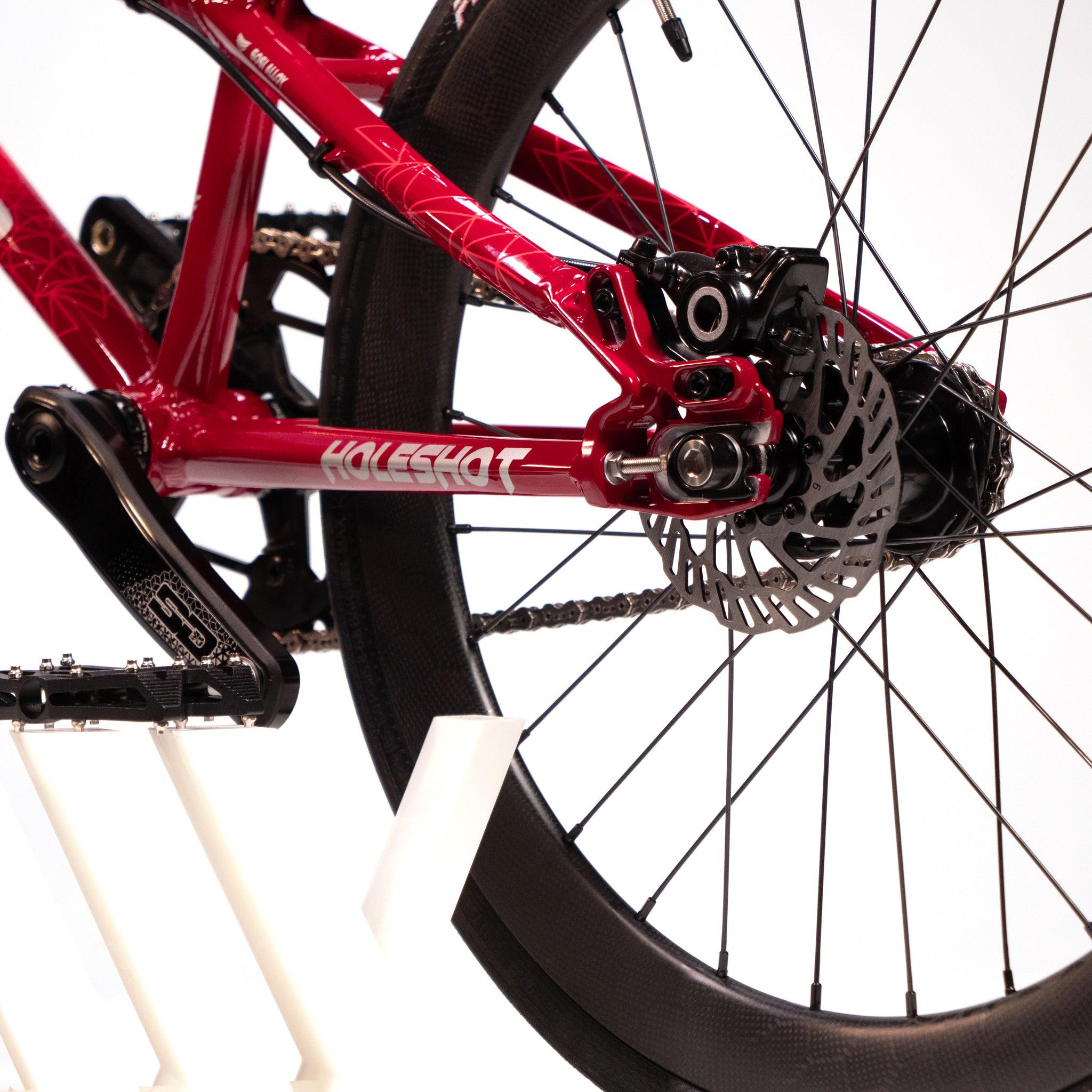 Close-up of the rear wheel and Onyx Pro HG disc hub of a red Meybo Holeshot Junior Custom Bike mounted on a white stand.