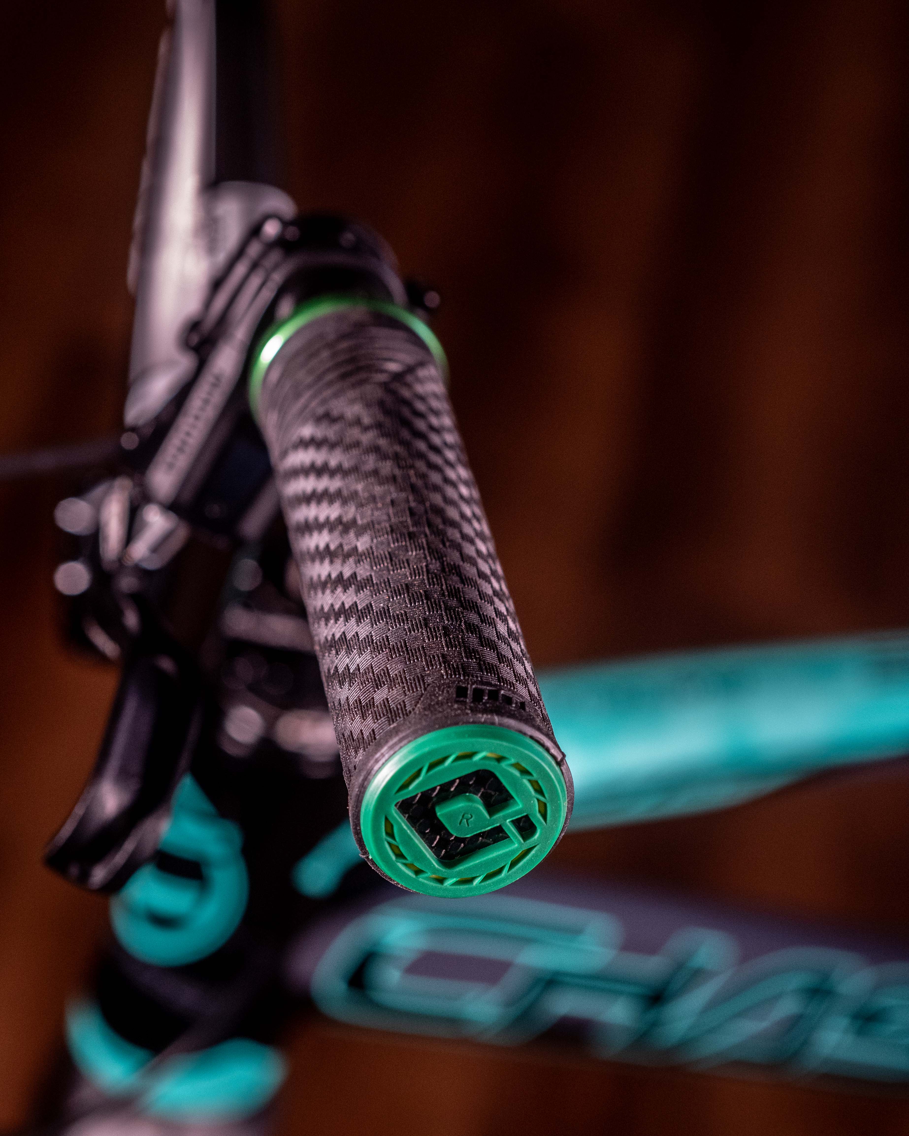 Close-up of the ODI CF Lock On Grips V2.1 Izaac Kennedy Signature, showcasing a carbon fiber pattern and a green end cap, set against a blurred background.