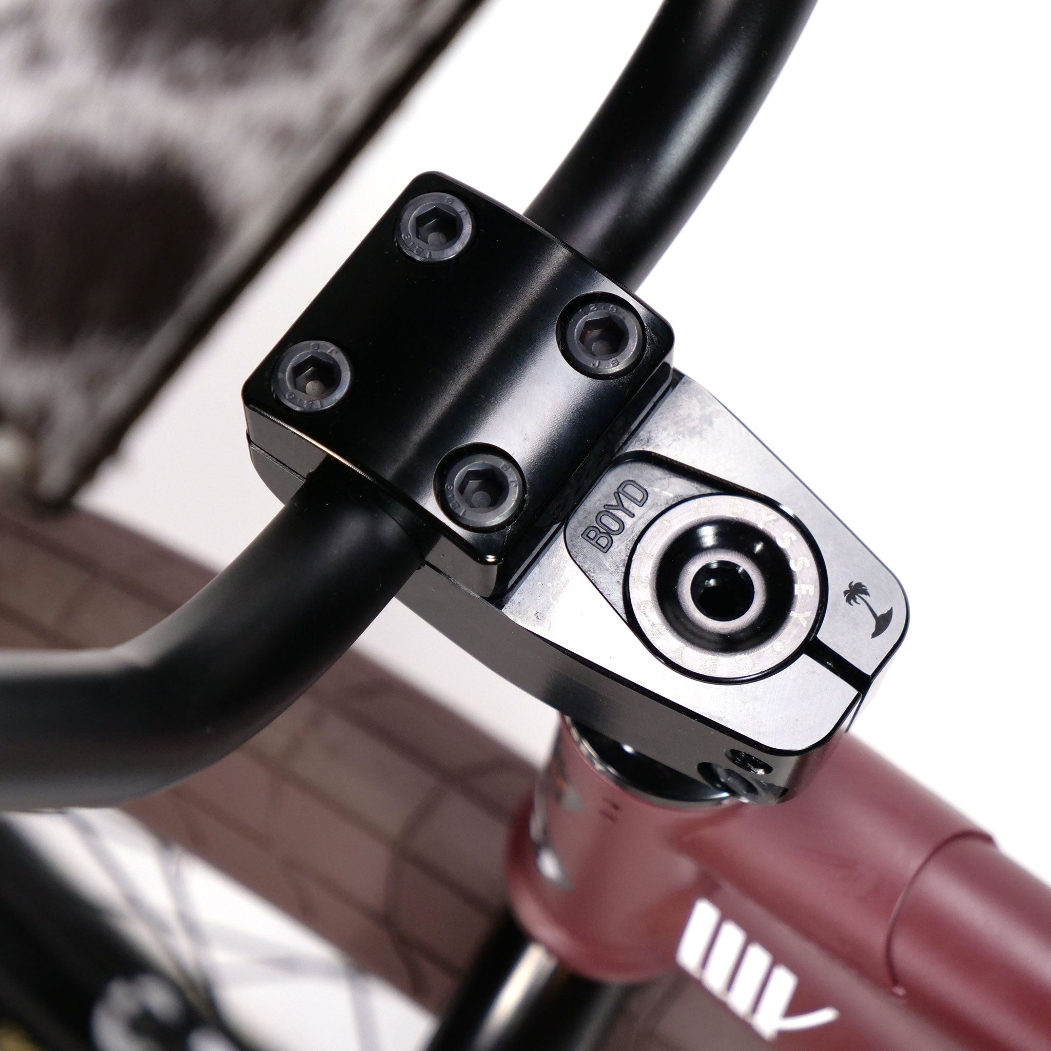 Close-up of a bicycle handlebar stem, featuring a black clamp with bolts and the brand name "BMXD" on a maroon frame, similar to the Federal CowBoyd Custom 20 Inch Bike's robust designs.