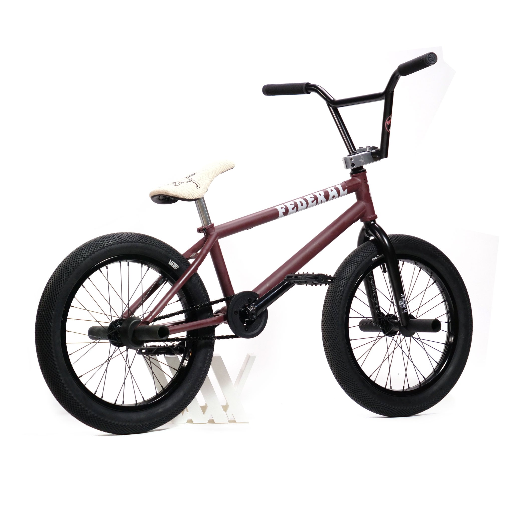 The Federal YUNGBOYD Custom 18 Inch Bike, featuring a red frame with a beige seat, black handlebars, and thick black tires, leans against a white stand, highlighting its freestyle custom design.