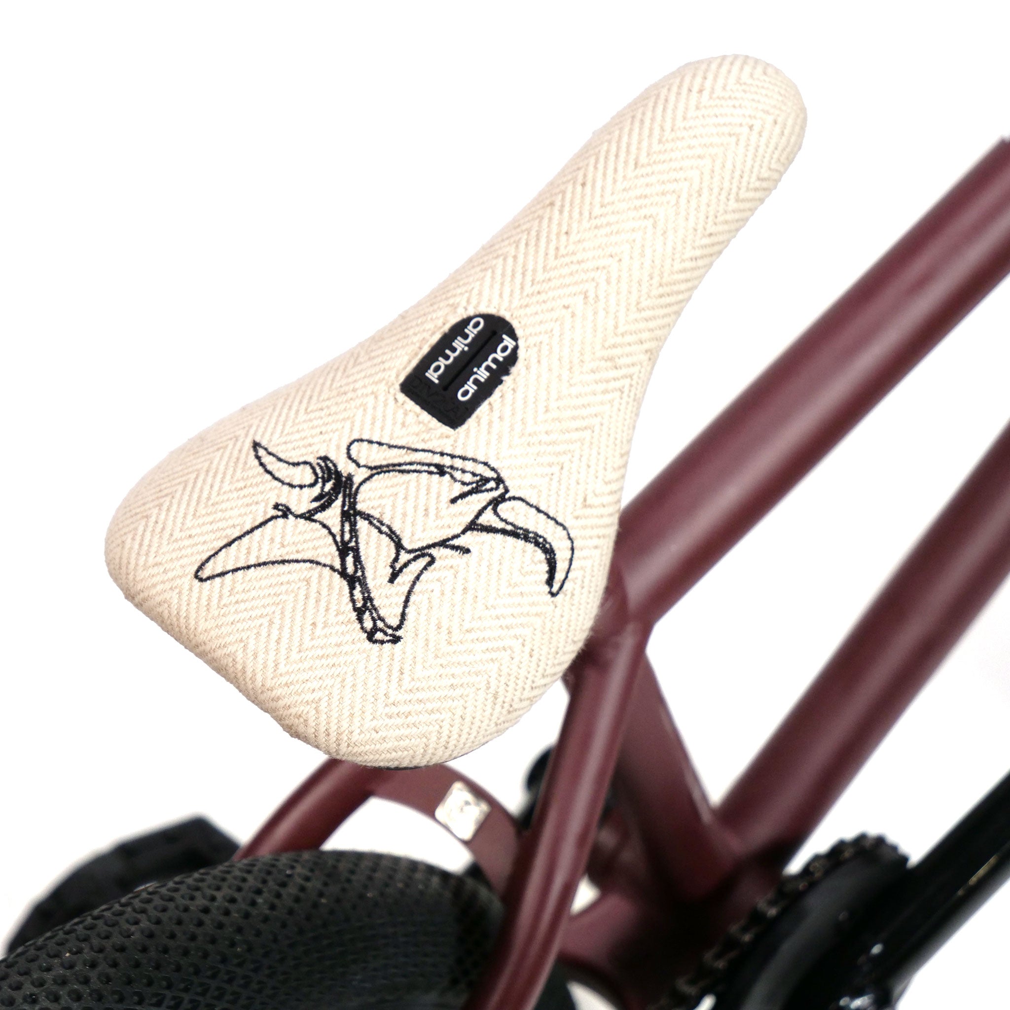 Close-up of a freestyle custom bicycle seat with a white herringbone pattern, featuring a black embroidered design. The seat is mounted on a maroon Federal YUNGBOYD Custom 18 Inch Bike, showcasing unique aftermarket parts for added flair.