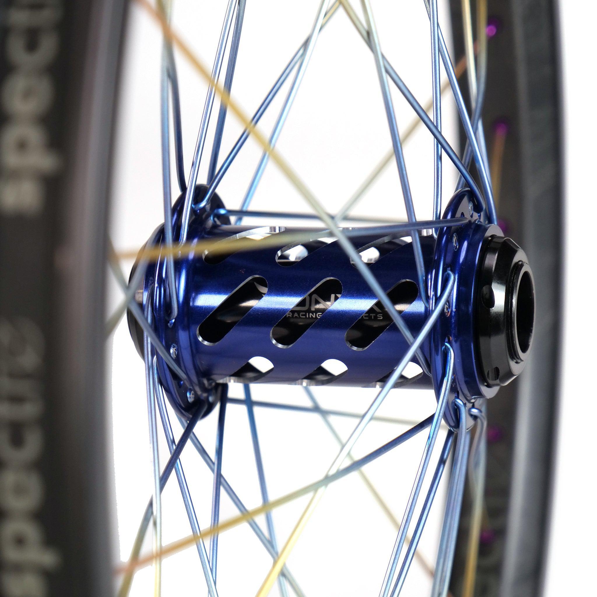 Close-up of the Onyx X Spectre Carbon Marble Sunset 20 Inch Wheelset with a metallic blue hub, black accents, titanium spokes, and black tire on sleek carbon fiber rims.