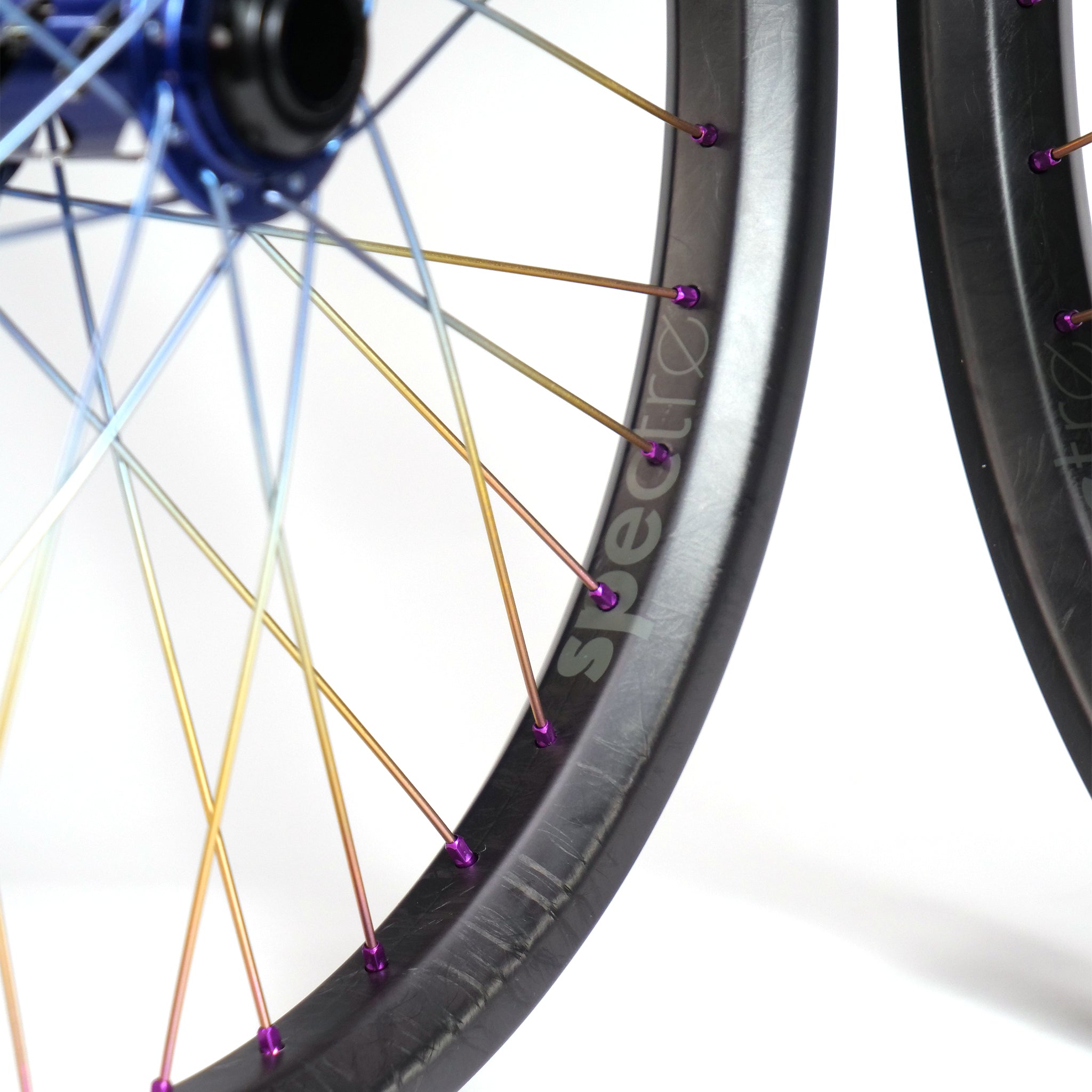 The Onyx X Spectre Carbon Marble Sunset 20-inch Wheelset boasts carbon fiber rims with rainbow titanium spokes and vibrant blue hubs, all accented by the sleek black rim featuring "svetrec" for a striking look.