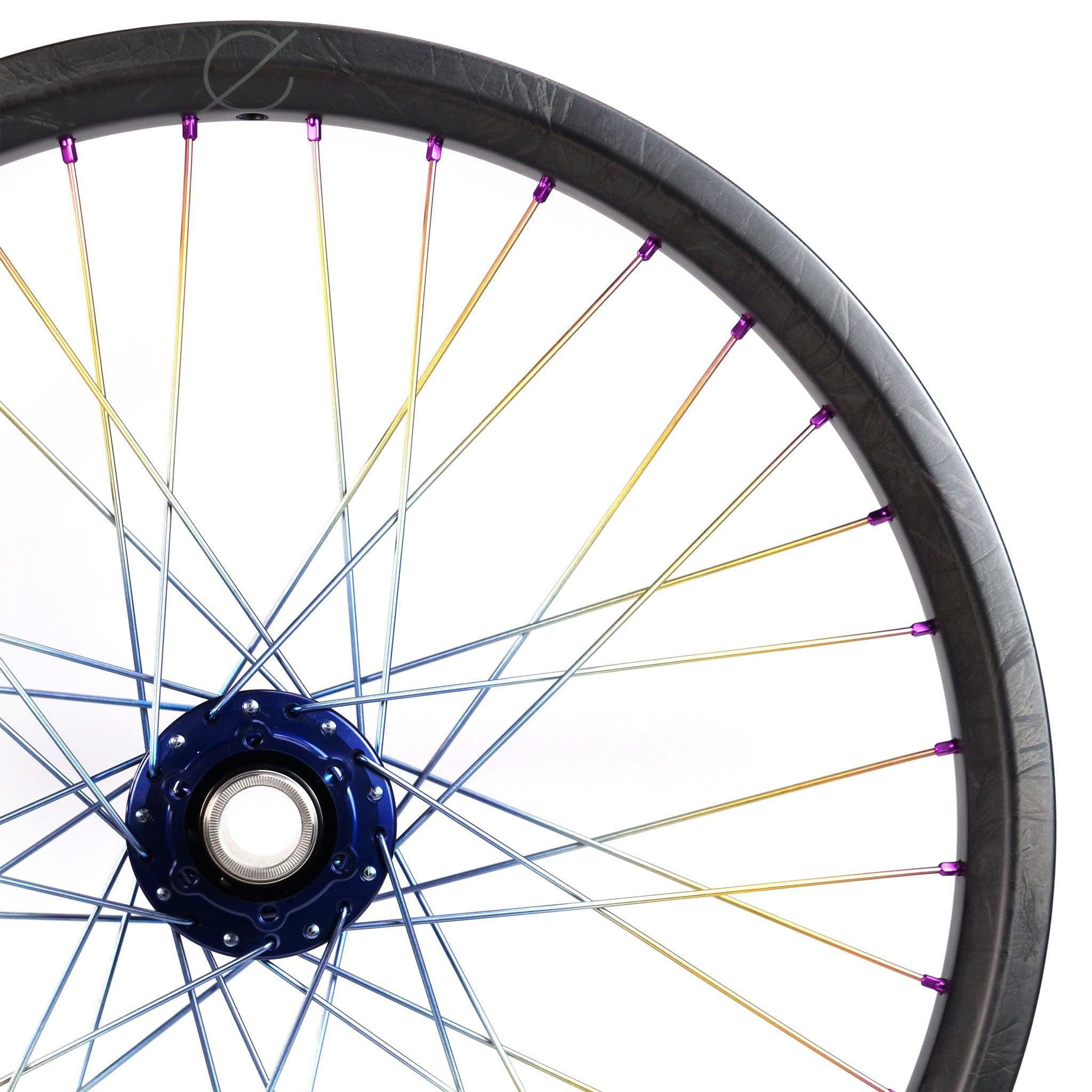 Against a white backdrop, the Onyx X Spectre Carbon Marble Sunset 20 Inch Wheelset reveals vivid titanium spokes and a glossy blue hub, highlighting expert craftsmanship.