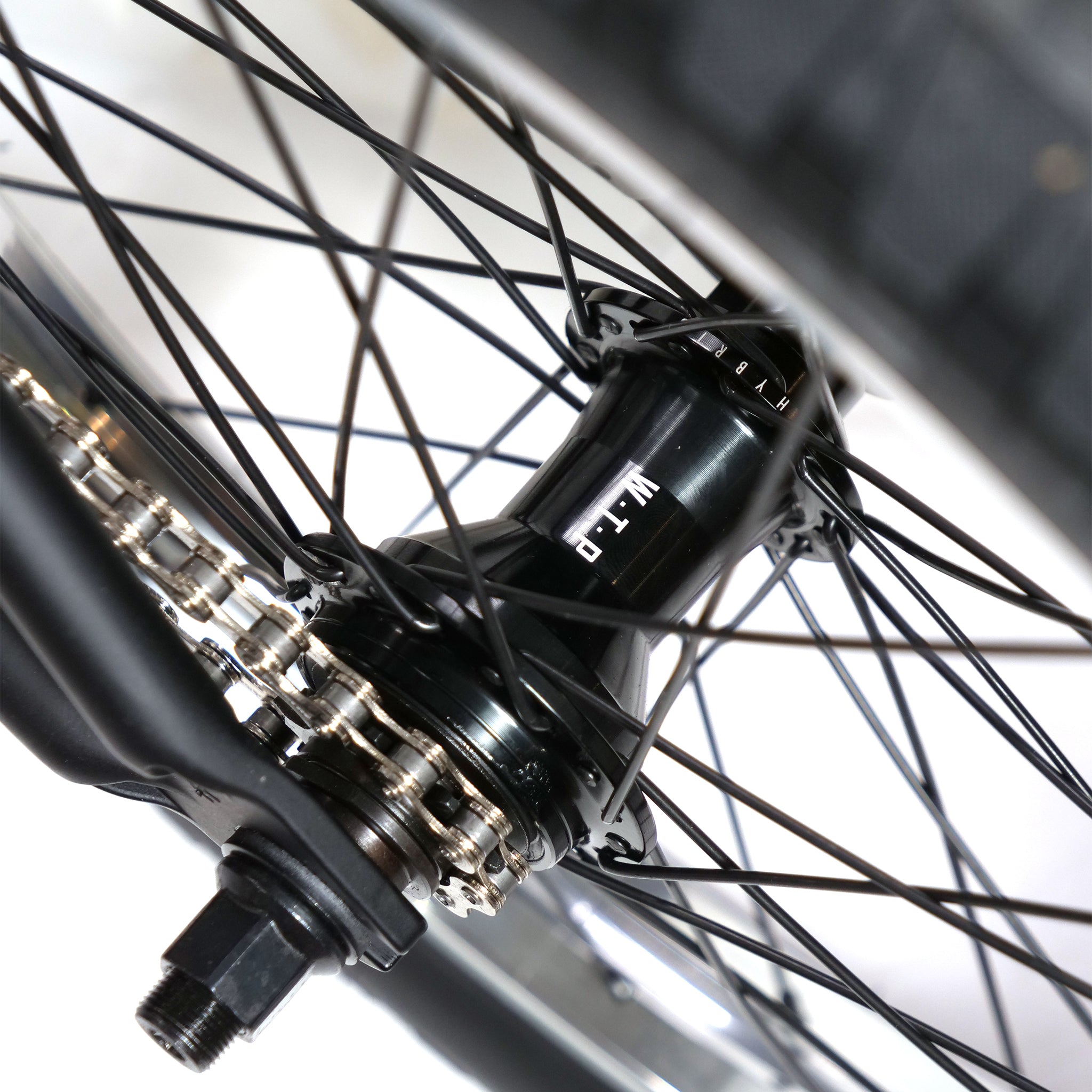 Close-up of the Fly Bikes Pajarito Custom 18 Inch BMX bike wheel featuring a black hub, spokes, and metal chain against a white background.