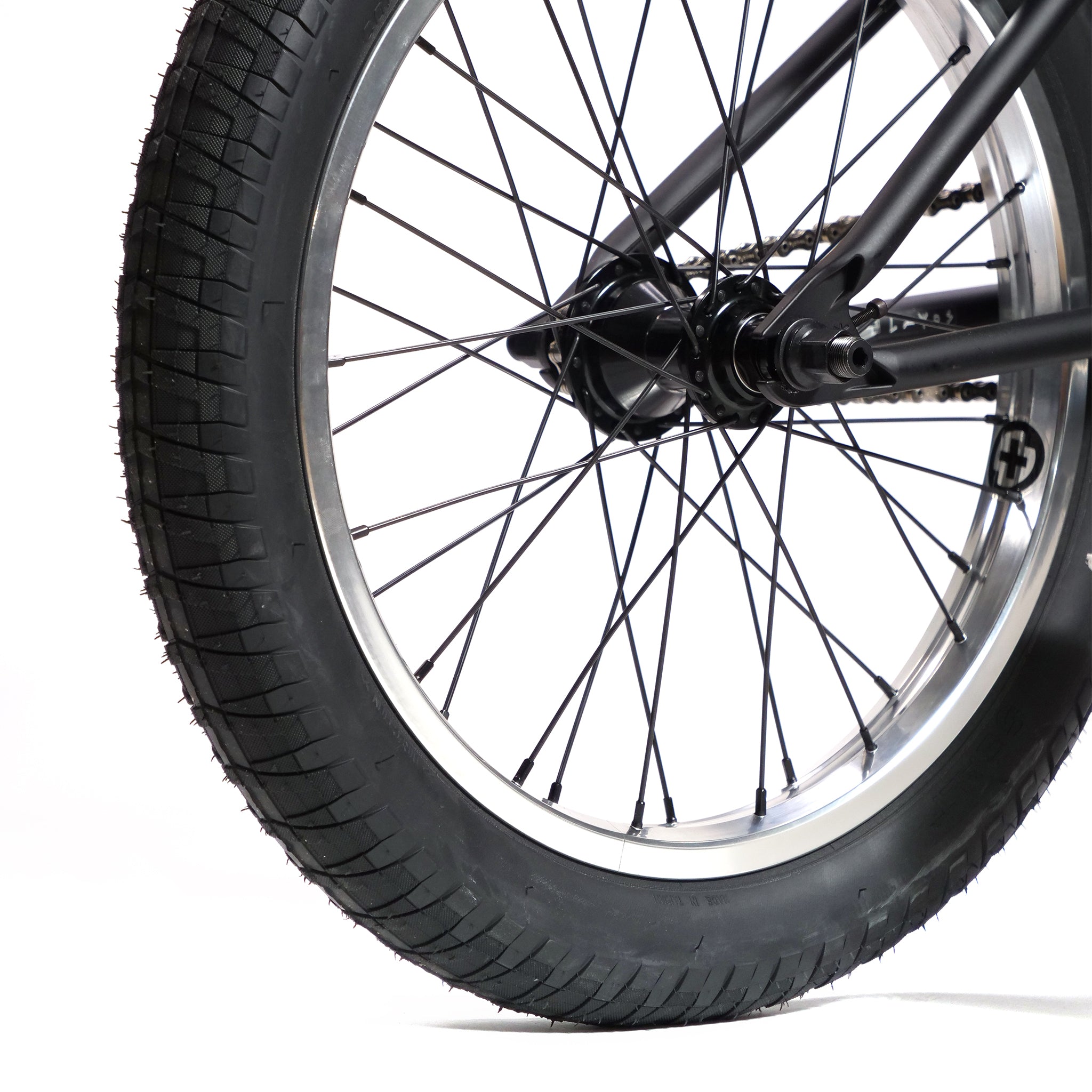 Close-up of the Fly Bikes Pajarito Custom 18 Inch BMX Bike's rear wheel, showcasing a black tire and metal spokes set against a white background.