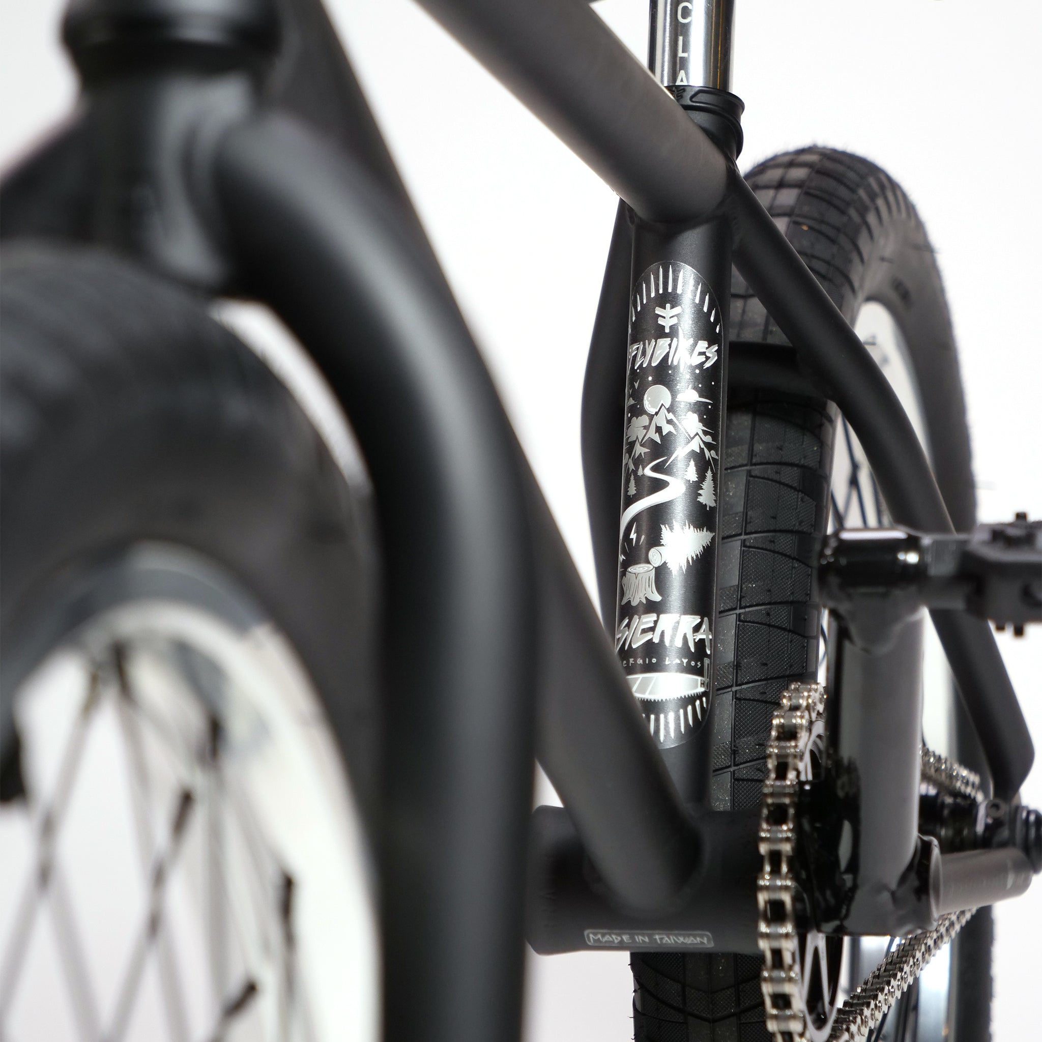 Close-up of a Fly Bikes Pajarito Custom 18 Inch BMX Bike's black frame with decorative graphics, displaying wheels and part of the chain.