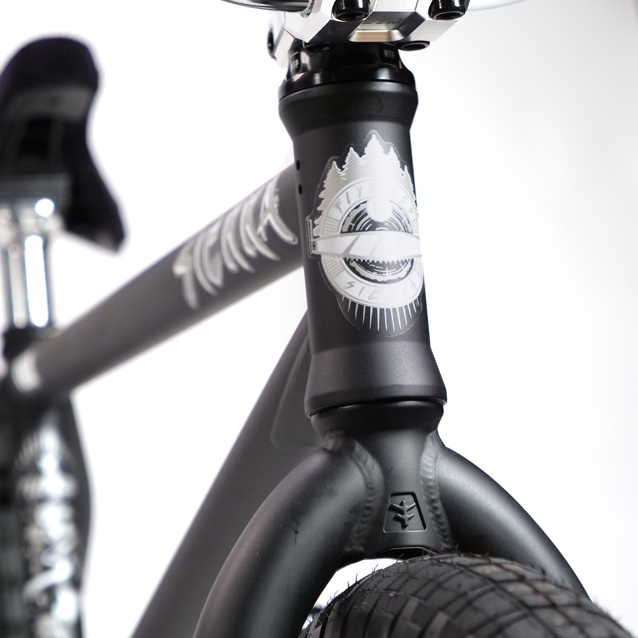 Close-up of the Fly Bikes Pajarito Custom 18 Inch BMX Bike's black frame, showing a mountain logo and a thick front tire with visible tread.