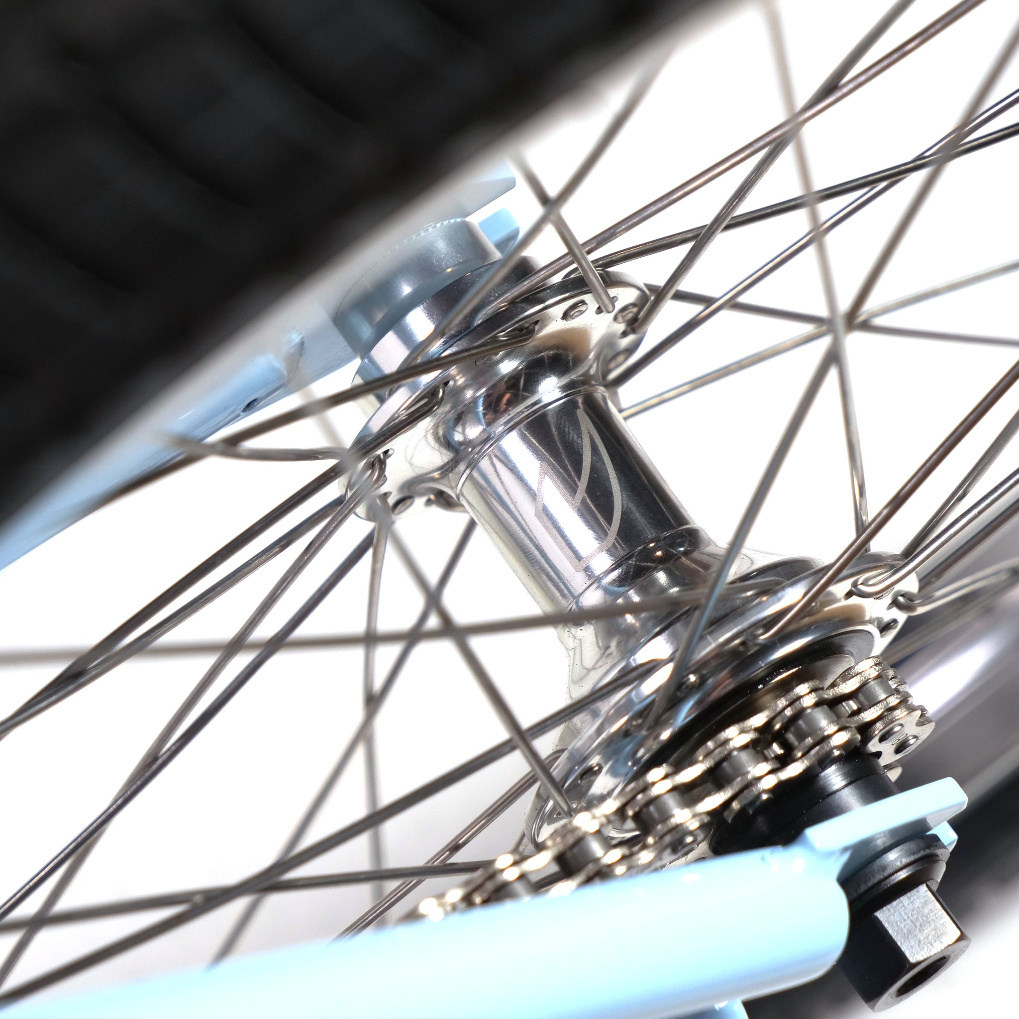 Close-up of the Hoffman TAJ Trend Adjacent Joy 20 Inch Custom Bike wheel hub with silver spokes and a light blue rim, echoing classic BMX freestyle designs by legends like Taj Mihelich. The prominent gear and axle highlight Hoffman bikes' craftsmanship.