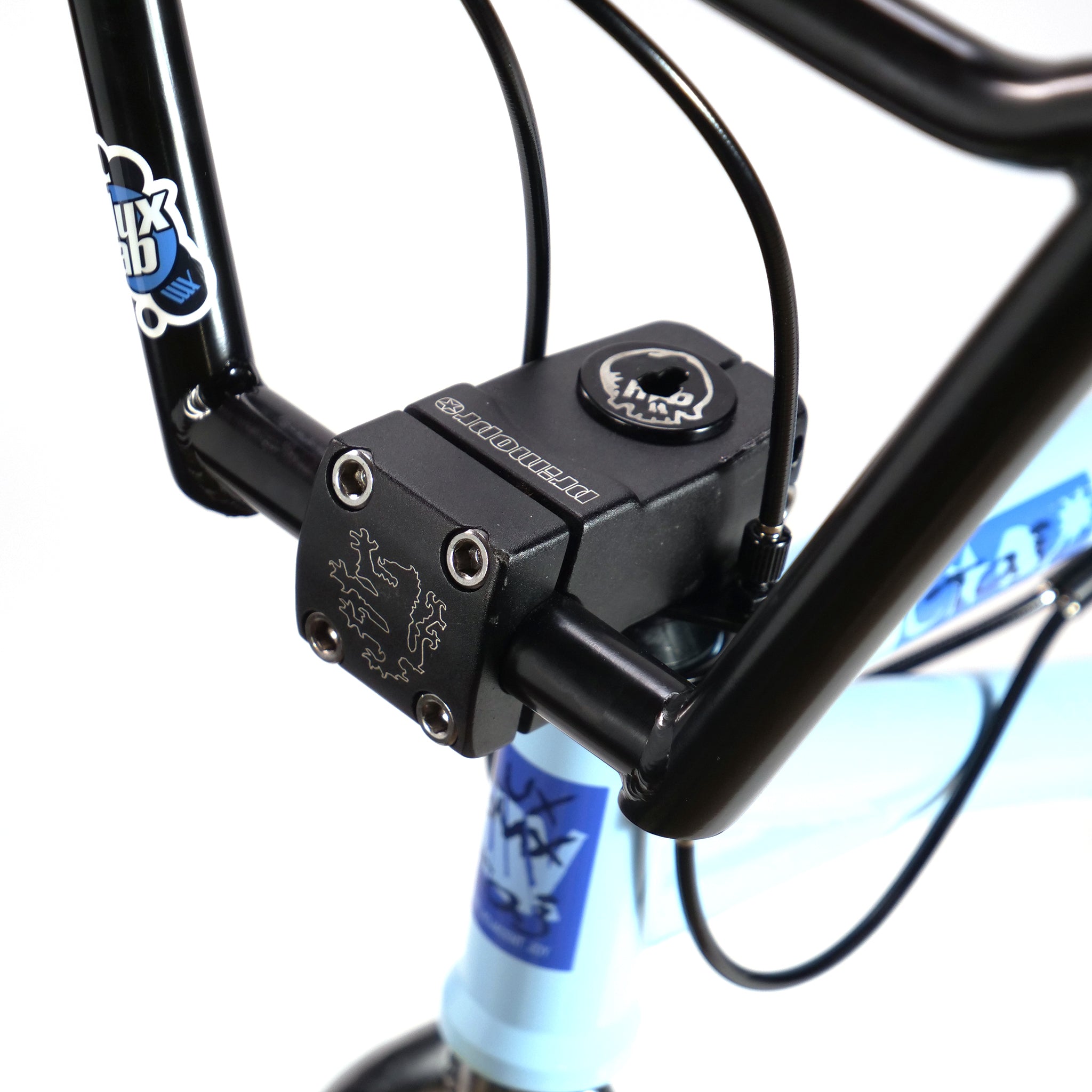 Close-up of a black handlebar and stem with logo on the Hoffman TAJ Trend Adjacent Joy 20 Inch Custom Bike, highlighting cables and a light blue frame—a tribute to Hoffman bikes' legendary craftsmanship.